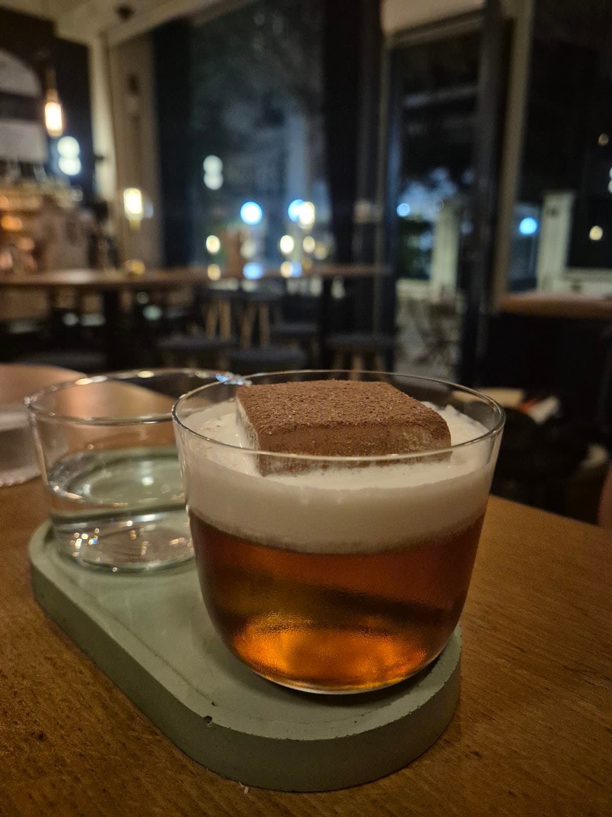 Close-up of cocktail with foam and garnish on a dimly lit bar table in Paris
