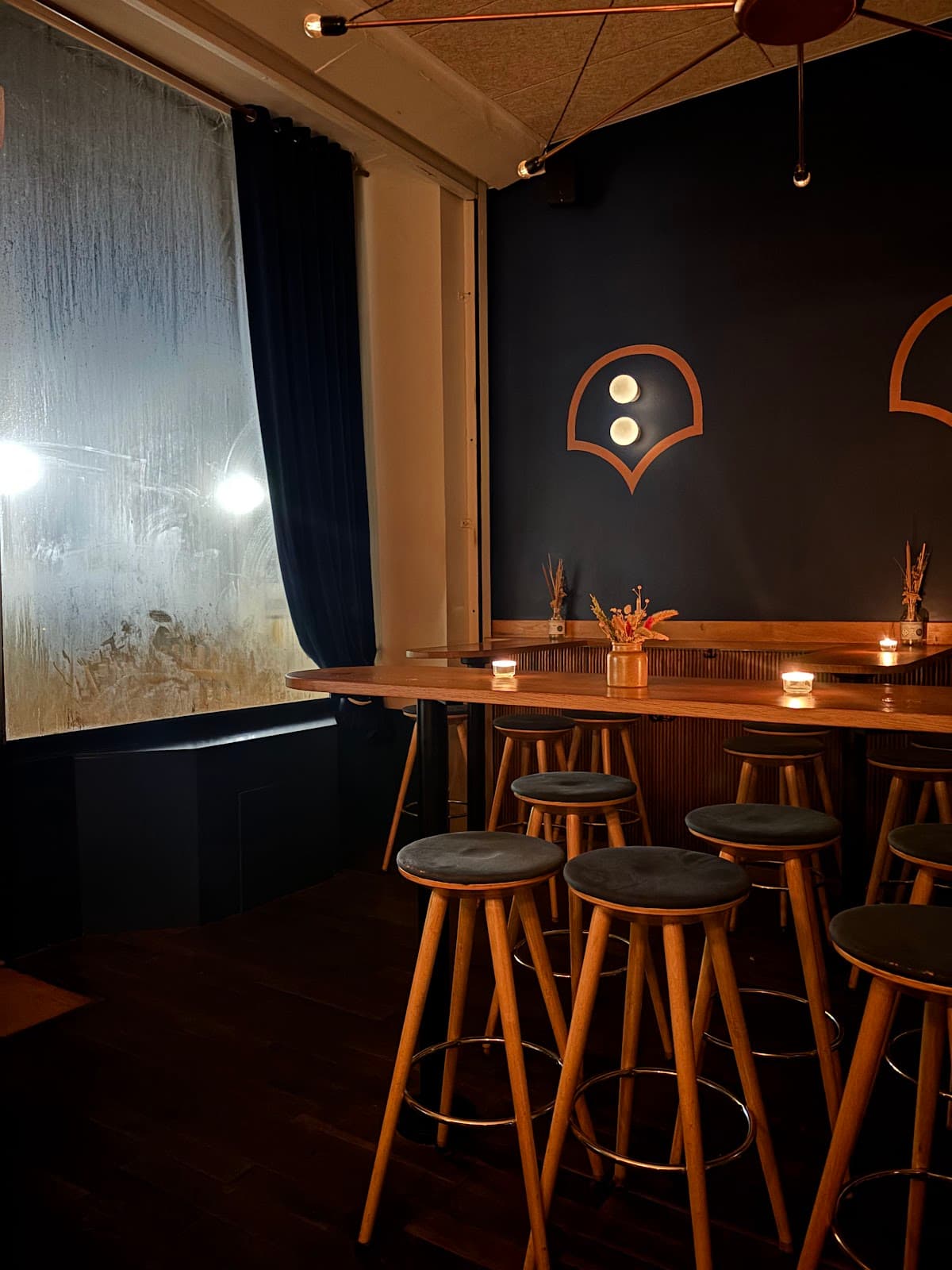 Cozy dimly lit bar interior with wooden stools and large window in Paris