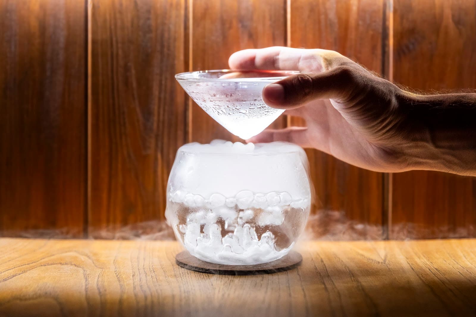 Hand holding glass above a smoky cocktail in a wooden setting in Lisboa