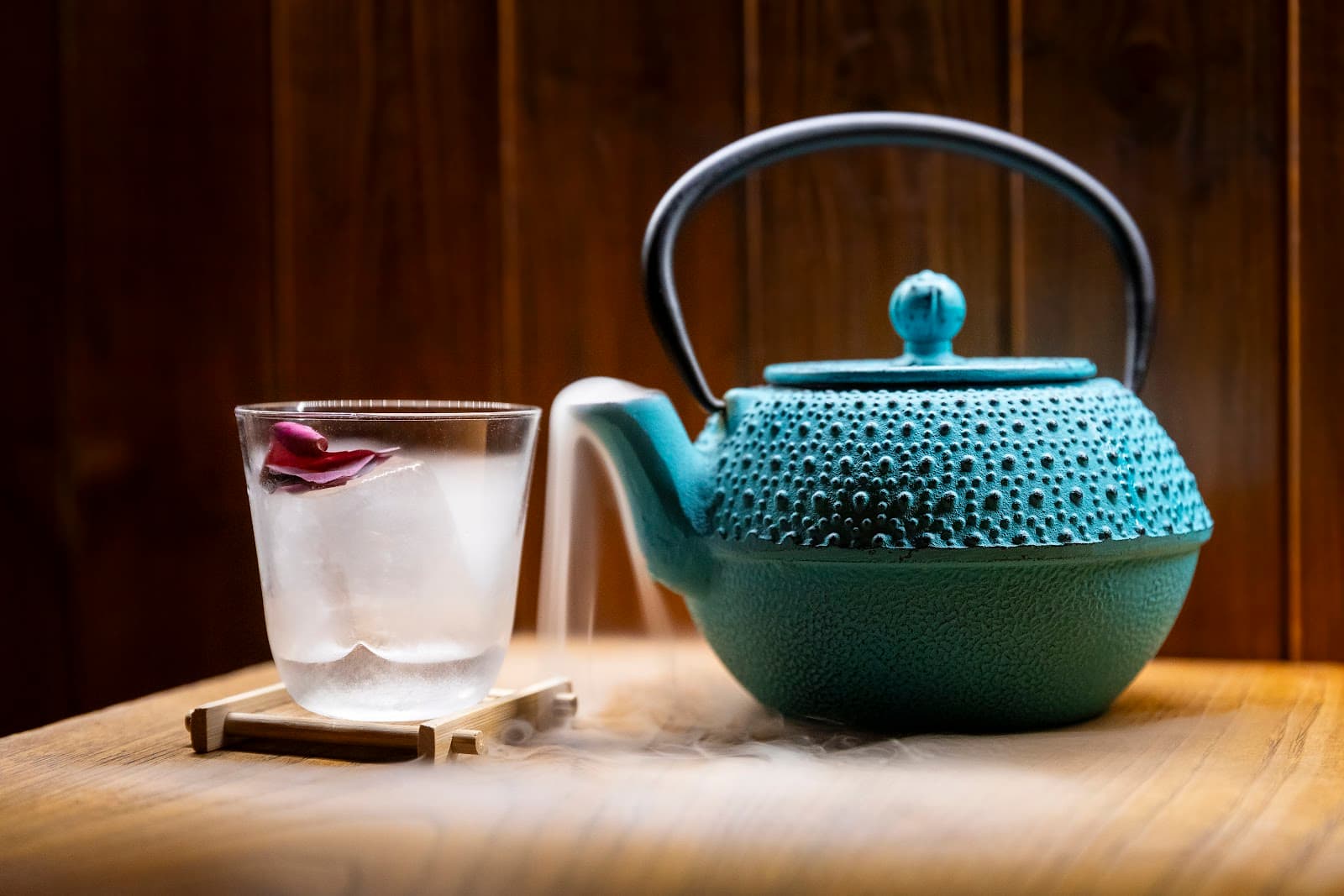 Elegant cocktail with rose petal and a teal teapot on a wooden table in Lisboa