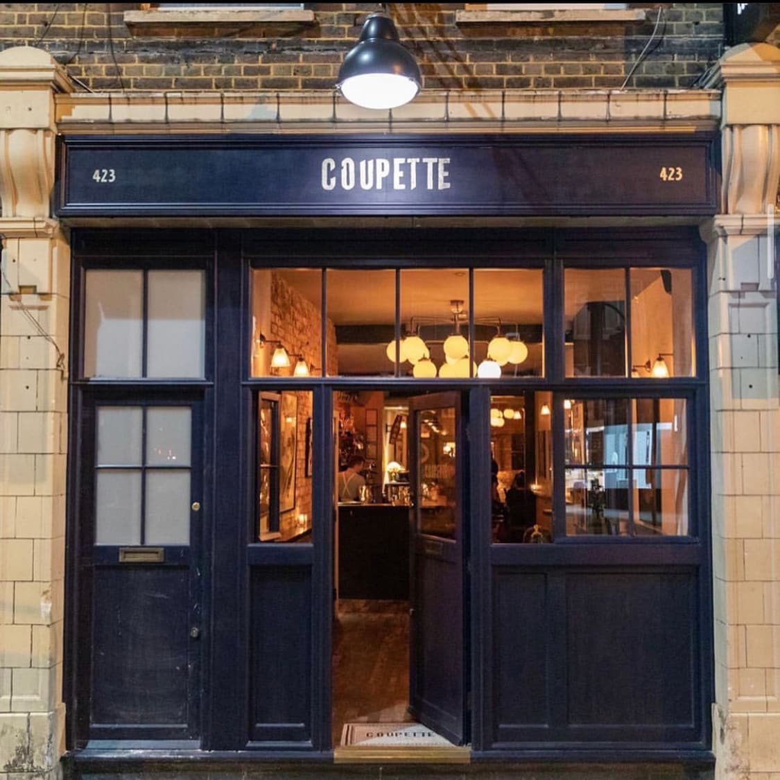 Well-lit exterior of Coupette bar with open doors and warm interior lighting