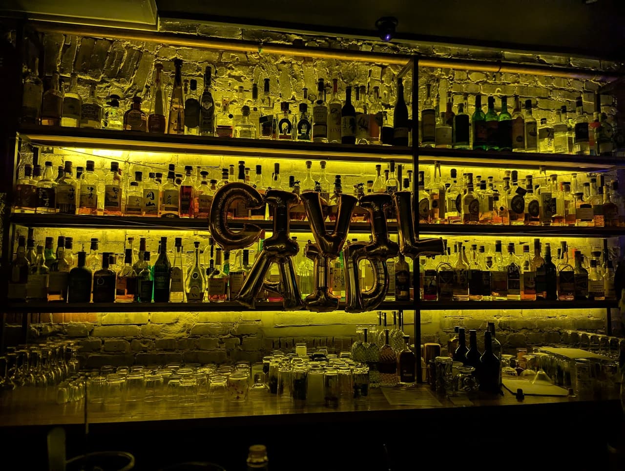 Bar counter with shelves of backlit liquor bottles, dim lighting in Toronto