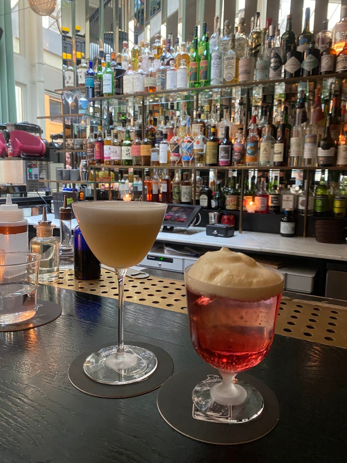Close-up of two cocktails on a bar with a backdrop of bottles in Paris