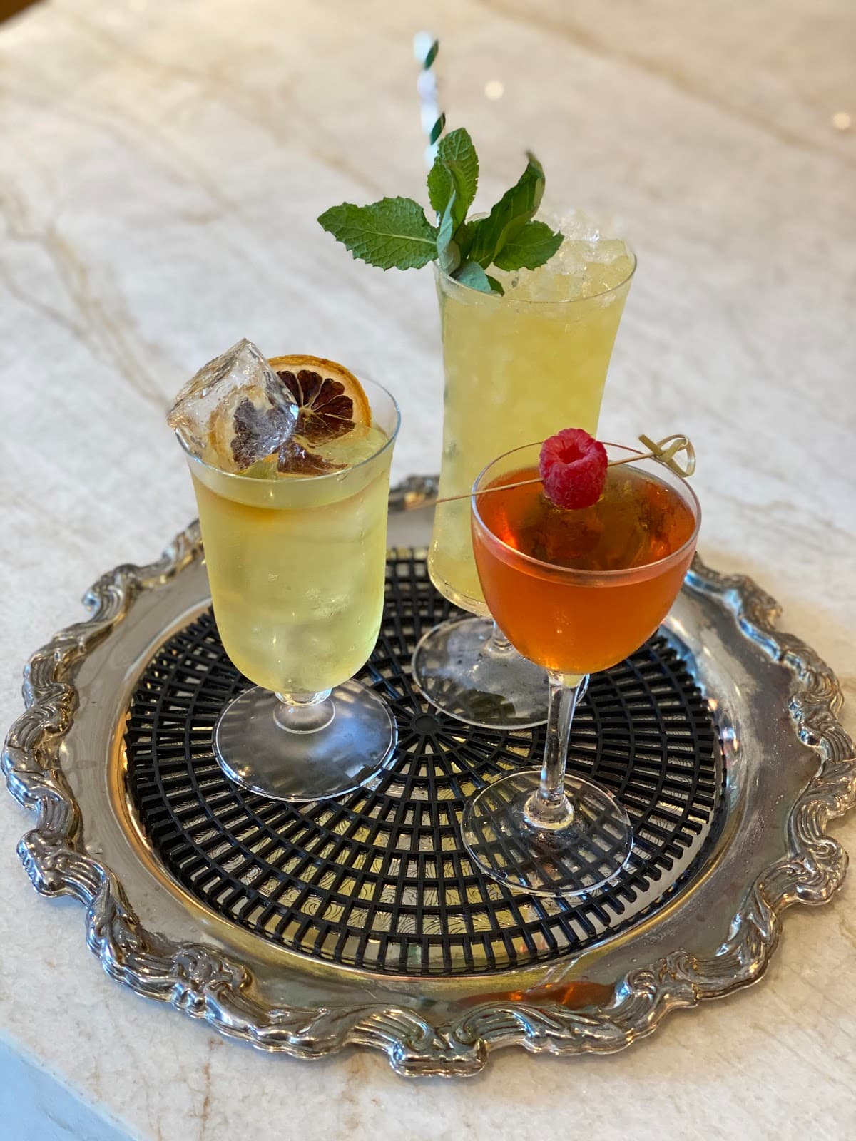 Three cocktails on a silver tray with garnishes and ice in New York