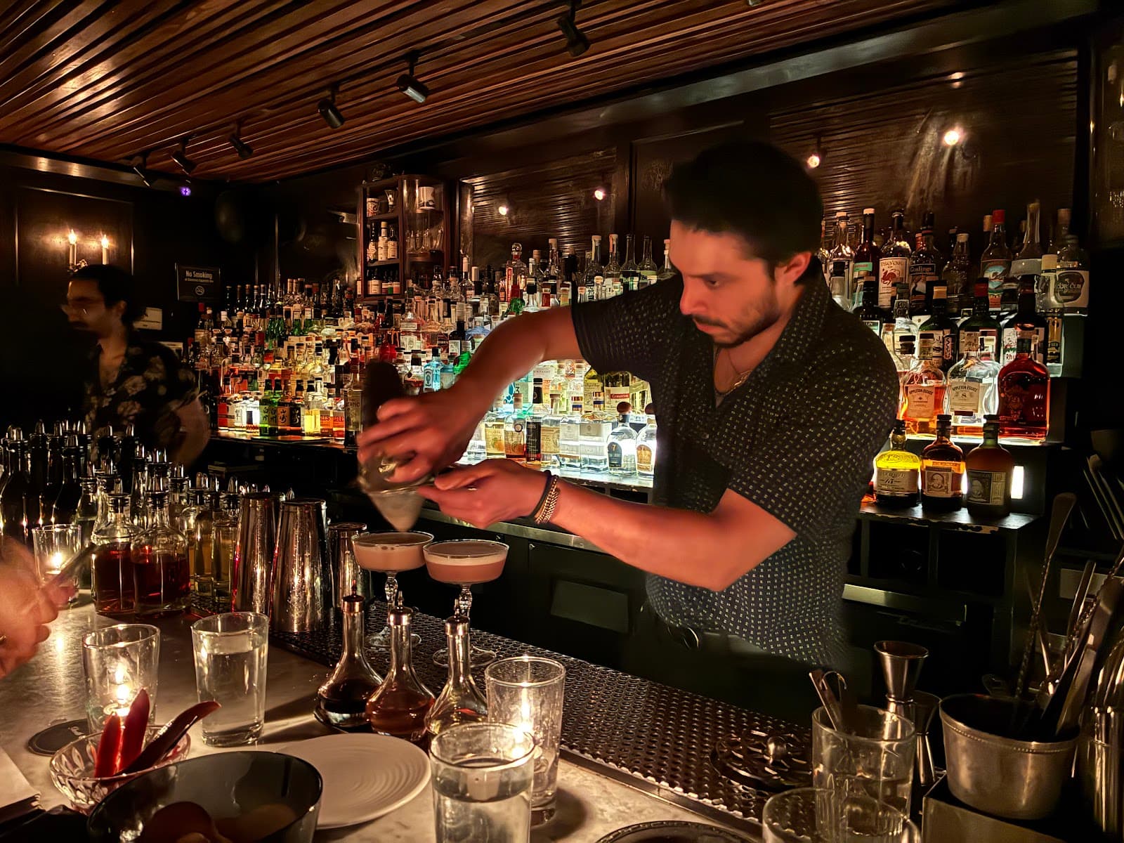 Bartender preparing cocktails with bottles in the background at a dimly lit bar in New York