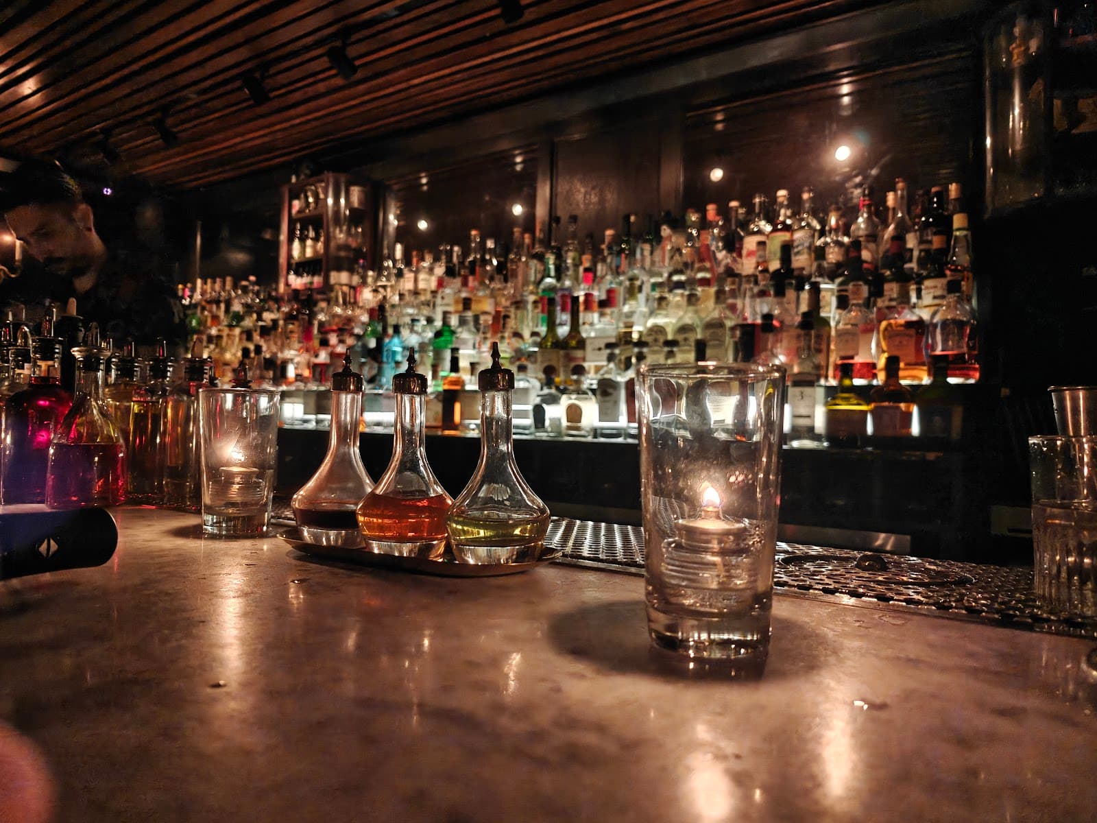 Candlelit bar counter with bottles and a bartender in dim lighting in New York