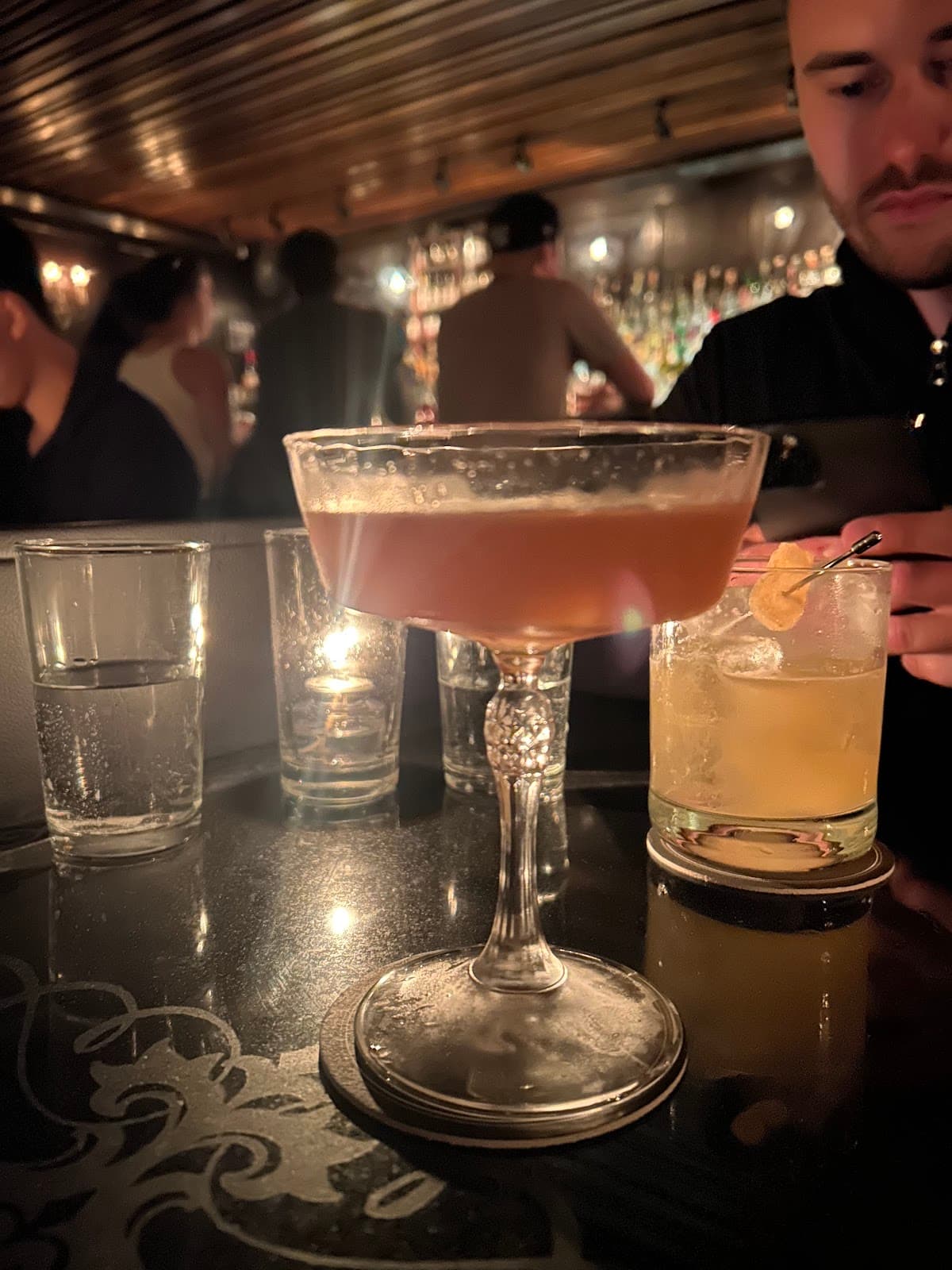 Cocktail glass on dimly lit table with people at bar in background in New York
