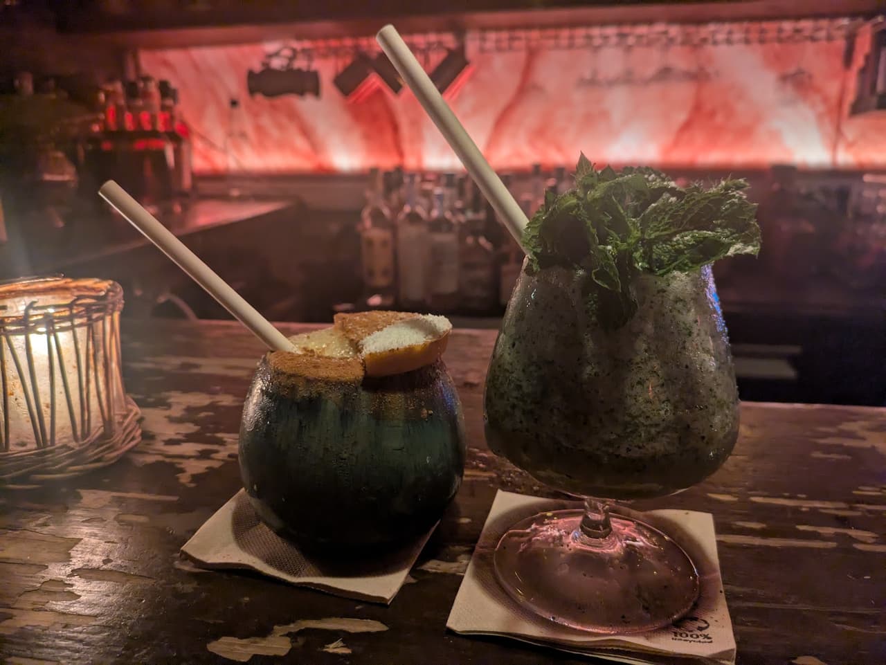Two cocktails with straws on a dimly lit bar counter in Paris