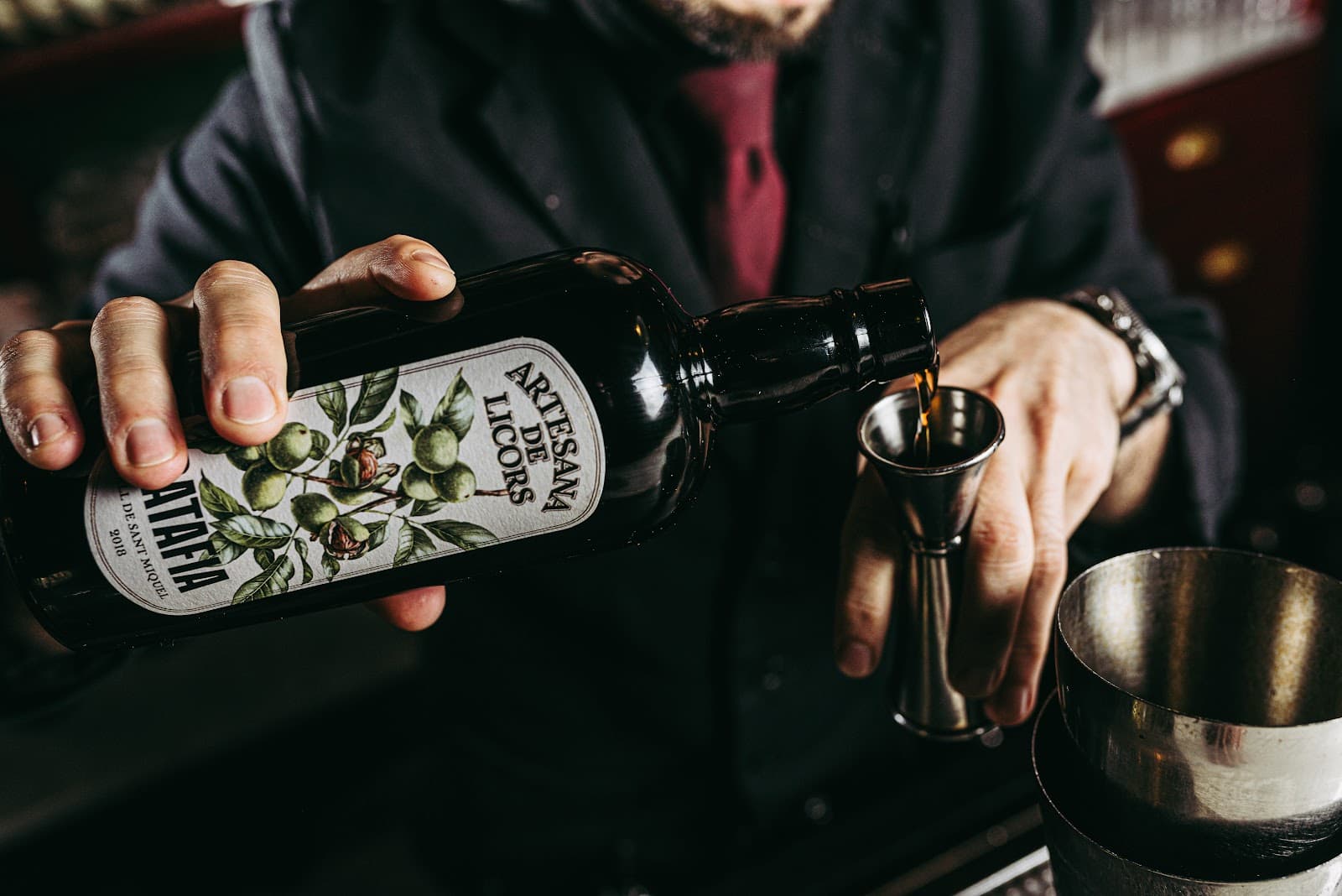 Bartender pouring artisanal liqueur into a jigger at a bar. in Barcelona