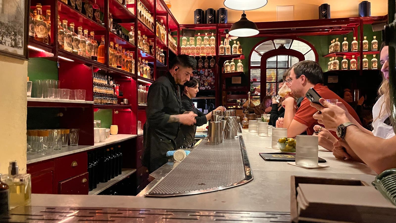 Bartender preparing drinks at a well-stocked bar with patrons seated in Barcelona