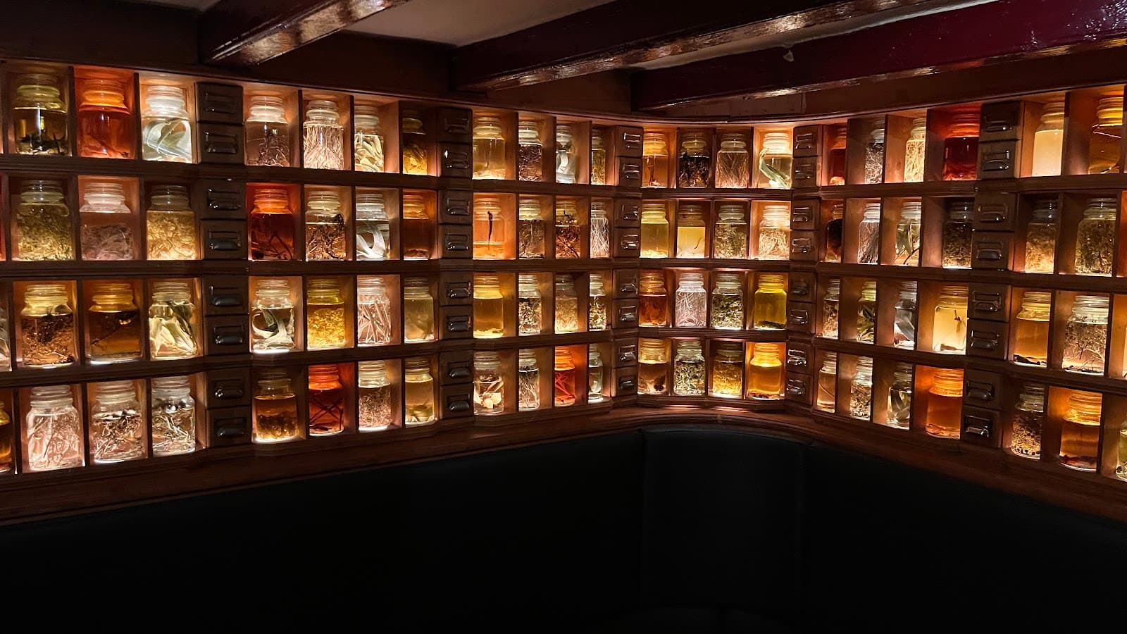 Wall of illuminated jars with herbs and spices in a dimly lit bar area in Barcelona