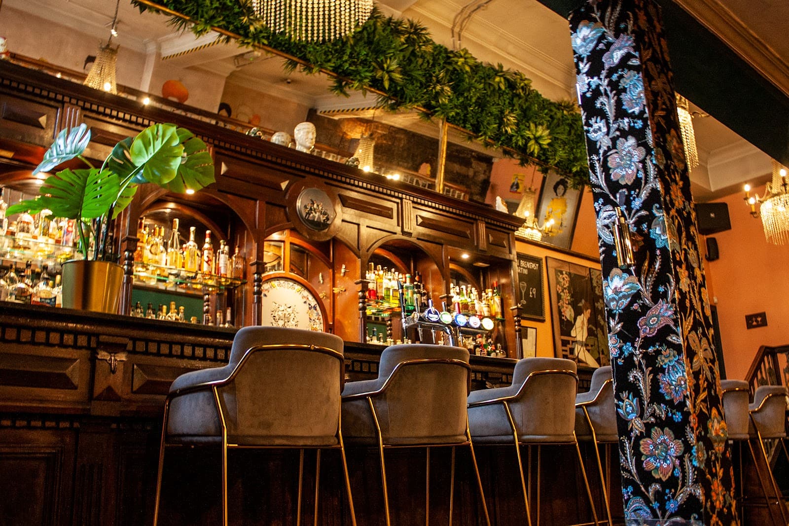 Elegant bar with velvet chairs, wooden counter, and hanging greenery
