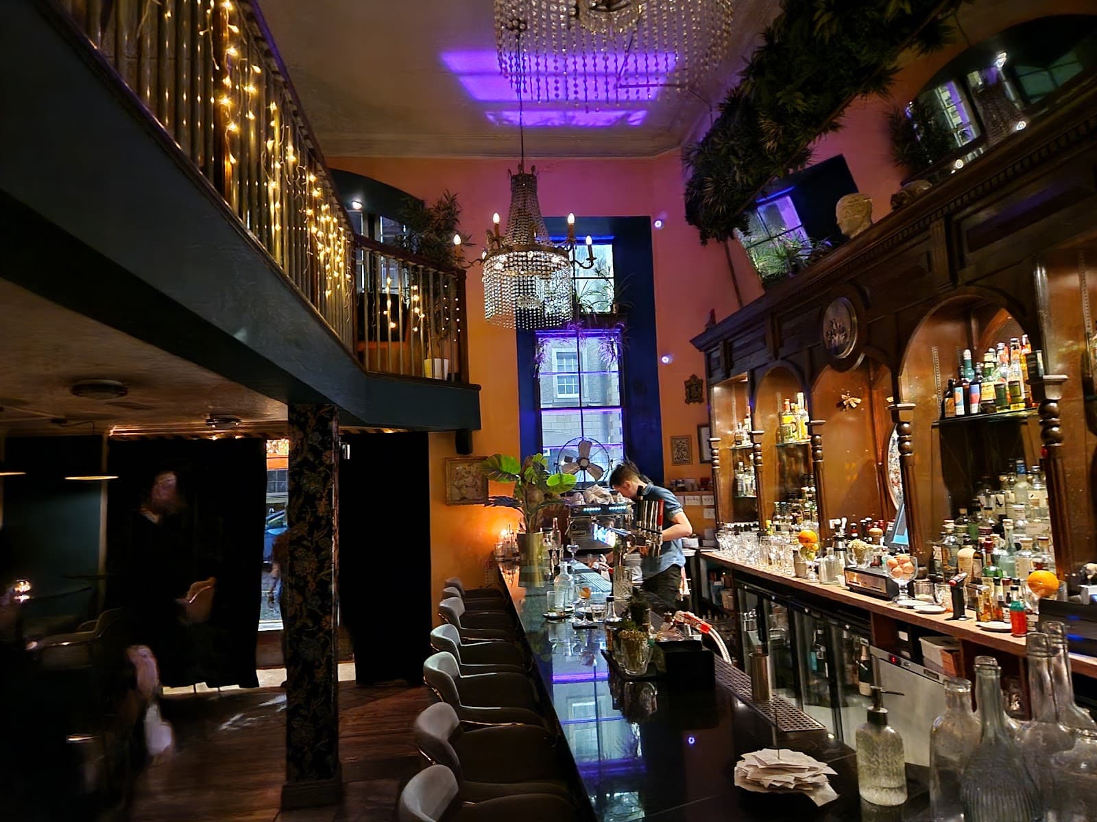 Well-lit bar with hanging lights and bartender at counter in Edinburgh