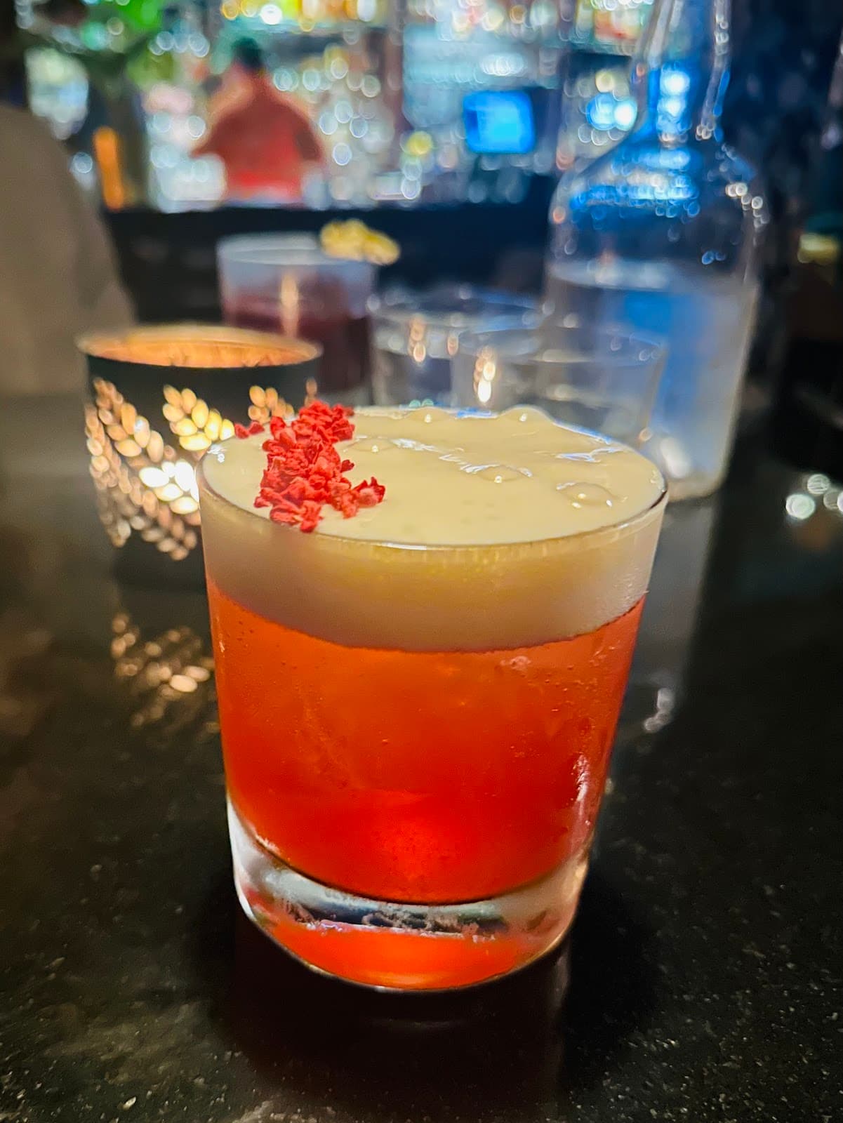 Vibrant red cocktail with foam on dark bar counter, blurred background in Edinburgh