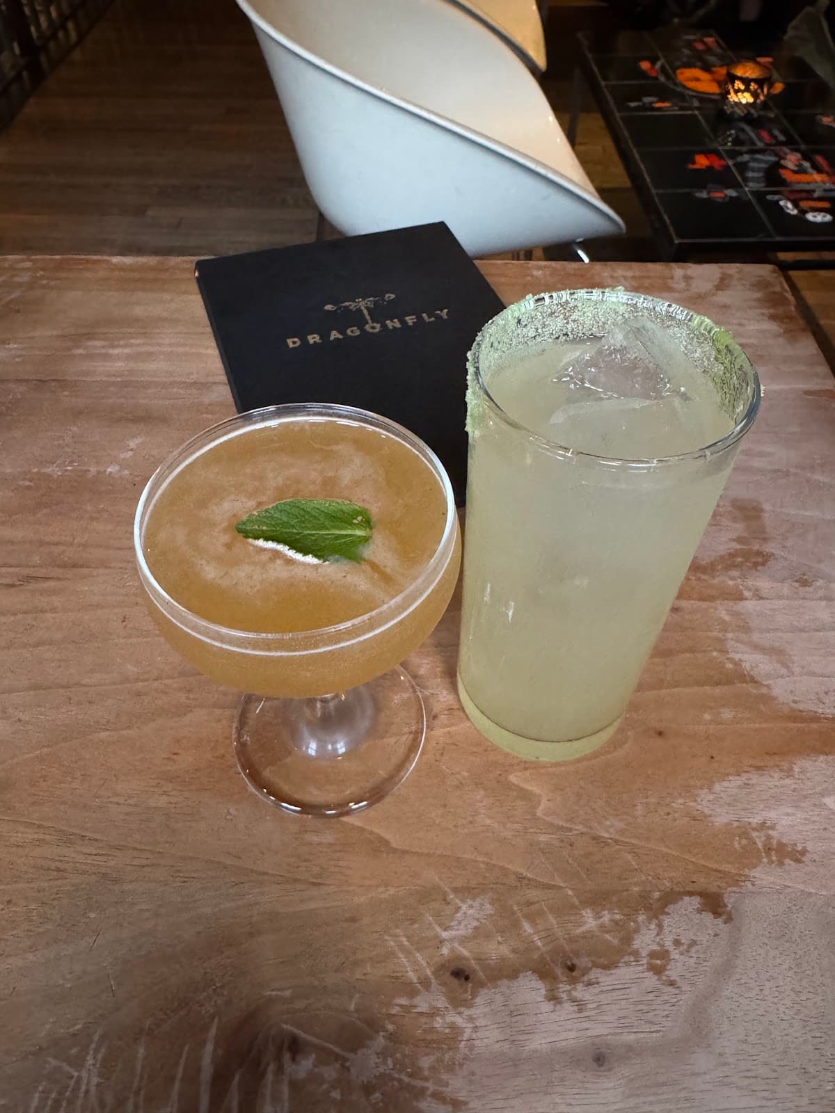 Two cocktails on a wooden table with a Dragonfly menu in Edinburgh