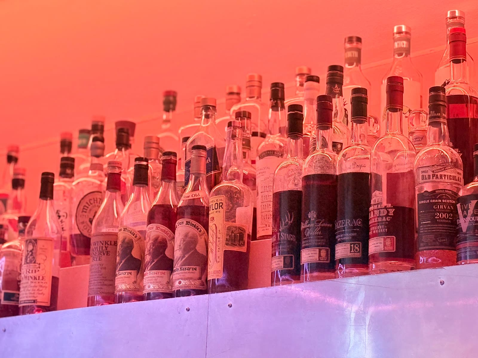 Close-up of a bar shelf with various liquor bottles under orange lighting in London