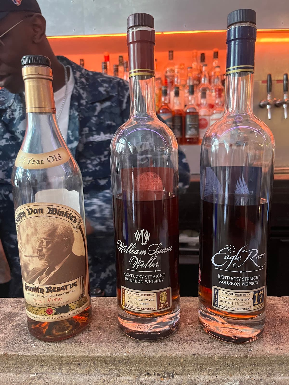 Close-up of three bourbon bottles at a bar counter in front of backlit shelves in London