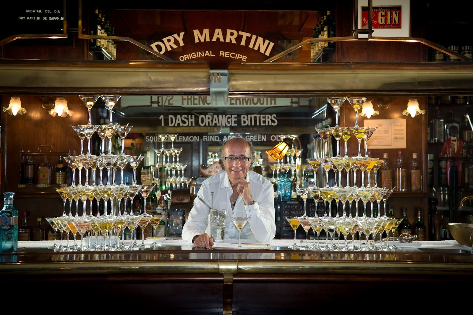 Bartender behind a pyramid of martini glasses at a bar.