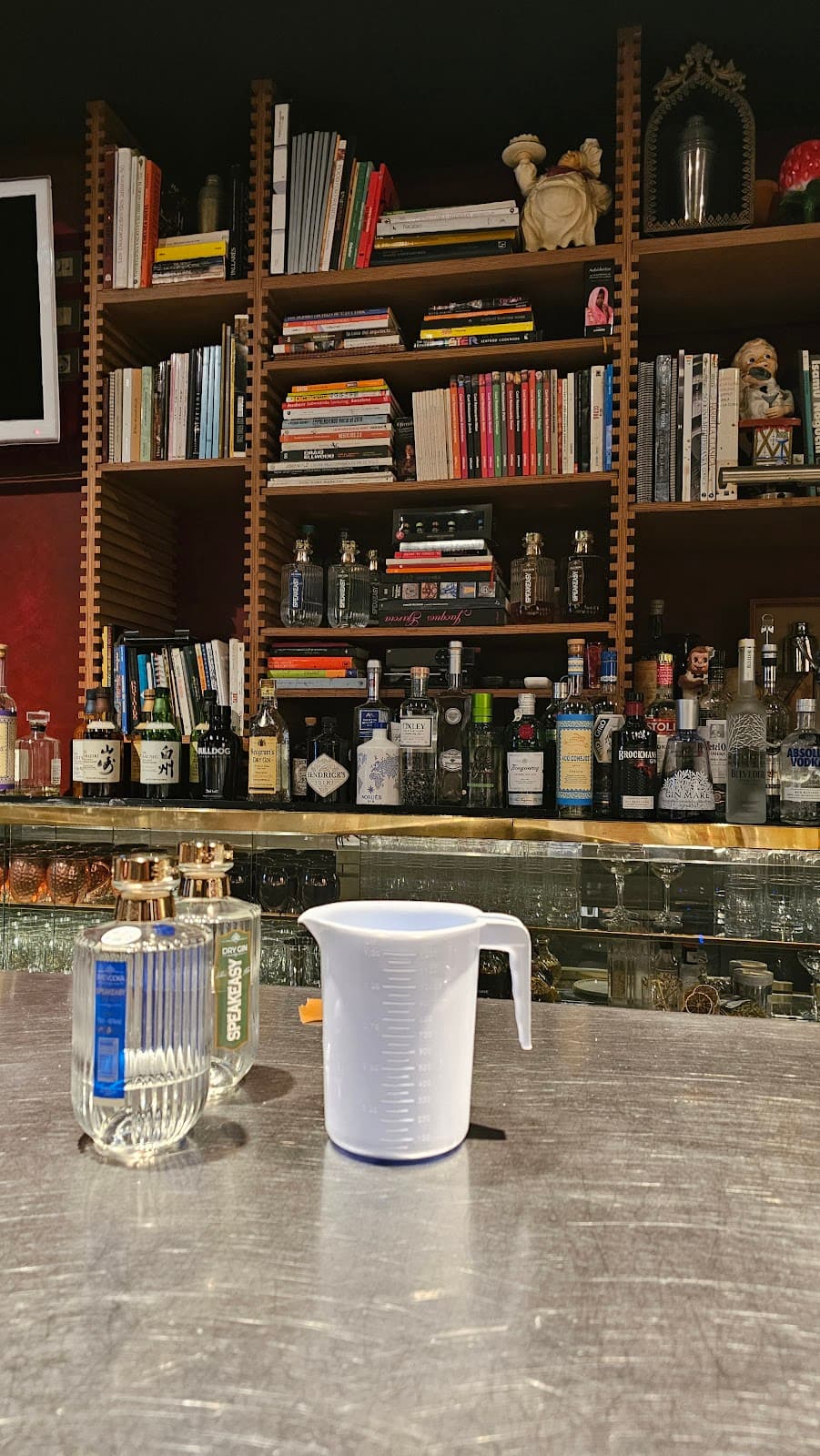 Bar counter with bottles, measuring cup, and books on shelves behind. in Barcelona