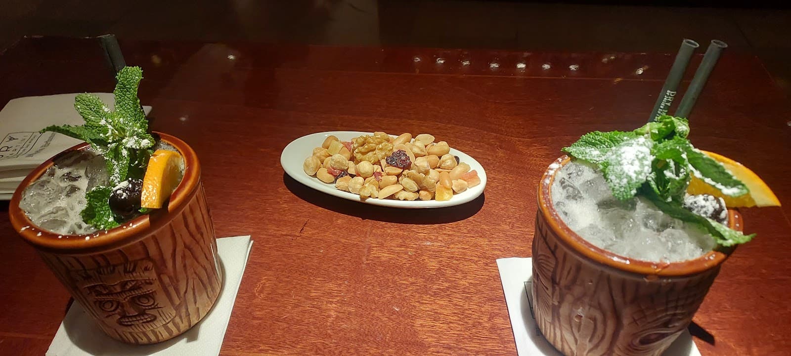 Two tiki cocktails with mint garnish and a bowl of nuts on a wooden table. in Barcelona