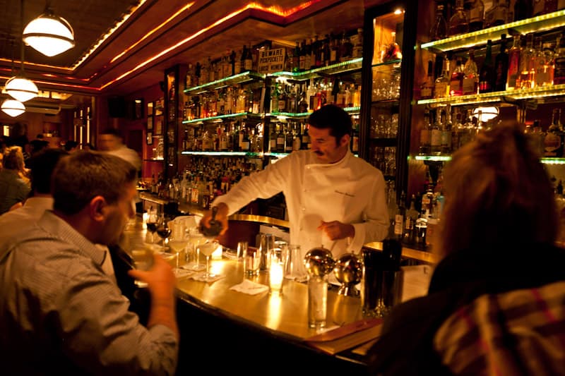 Bartender preparing cocktails at a well-stocked bar in a dimly lit setting