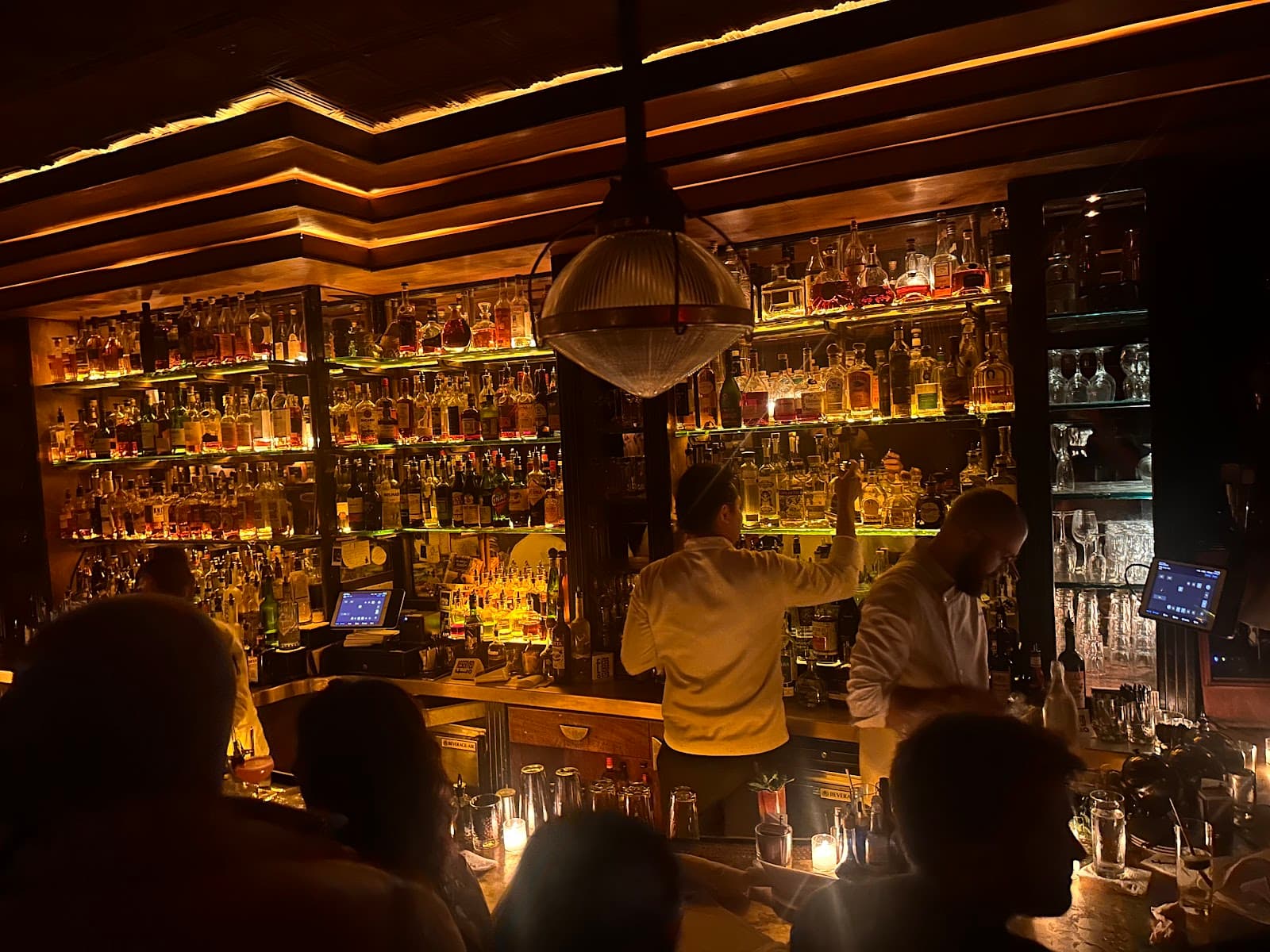 Bartenders working behind a well-lit bar with numerous bottles on shelves in New York