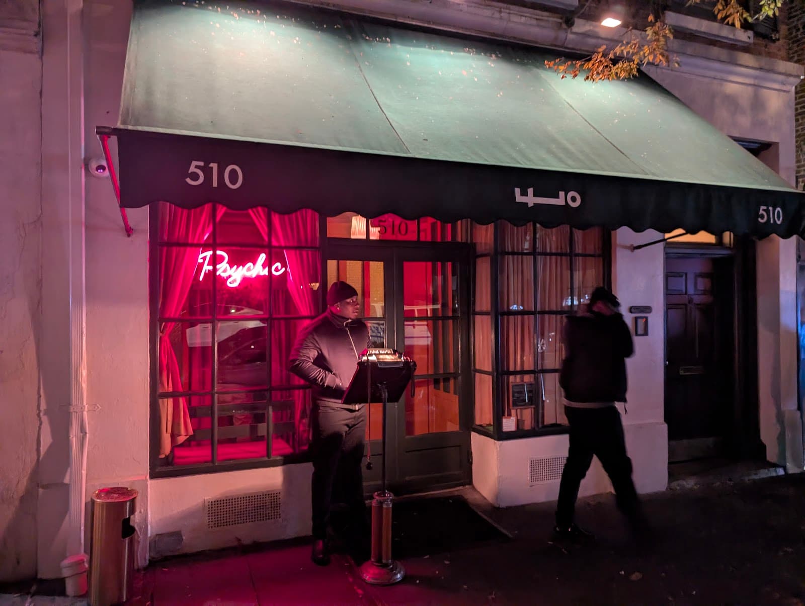 Exterior of a dimly lit venue with a red neon psychic sign and green awning in New York