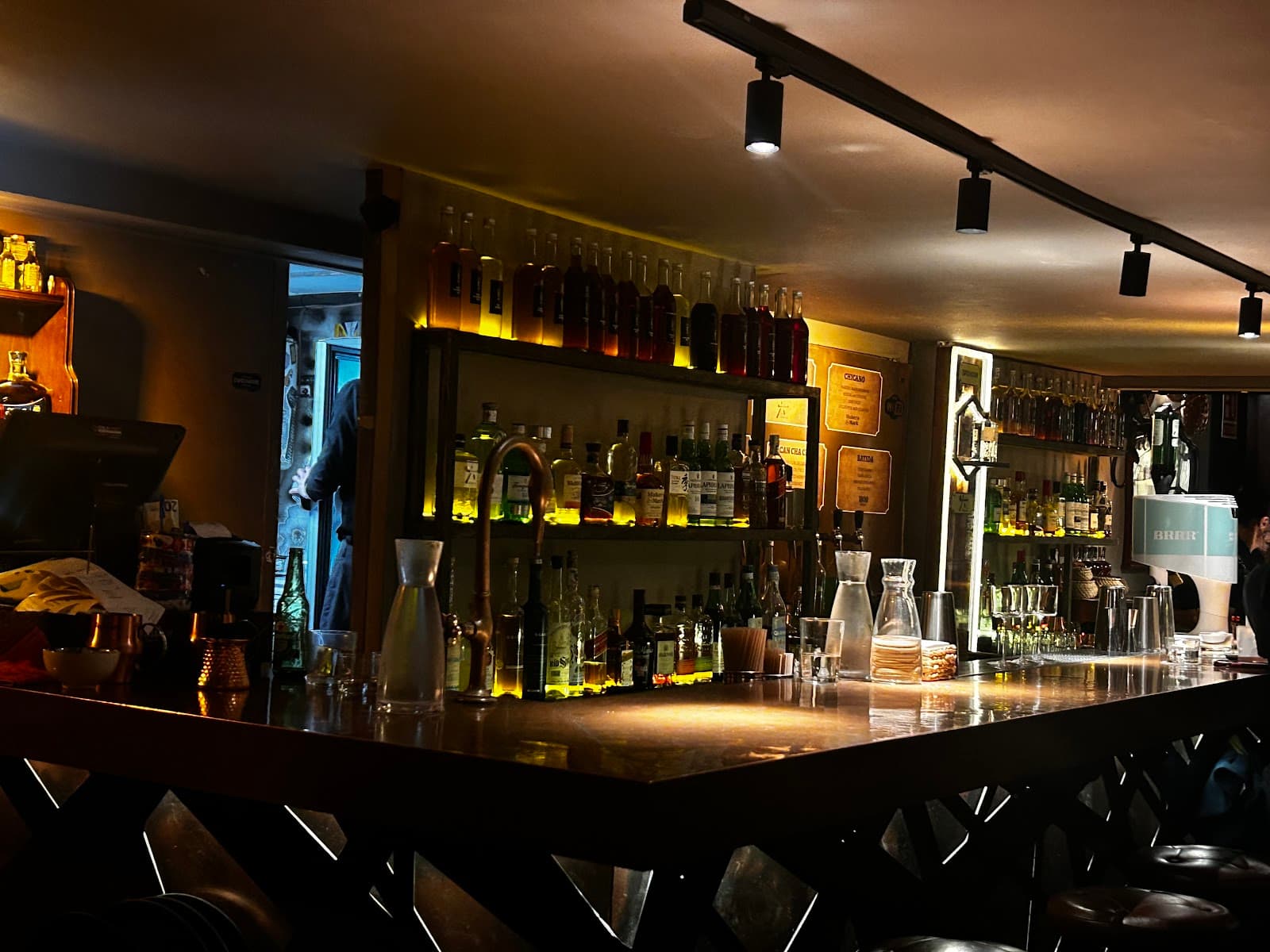 Dimly lit bar with bottles on shelves and a polished counter