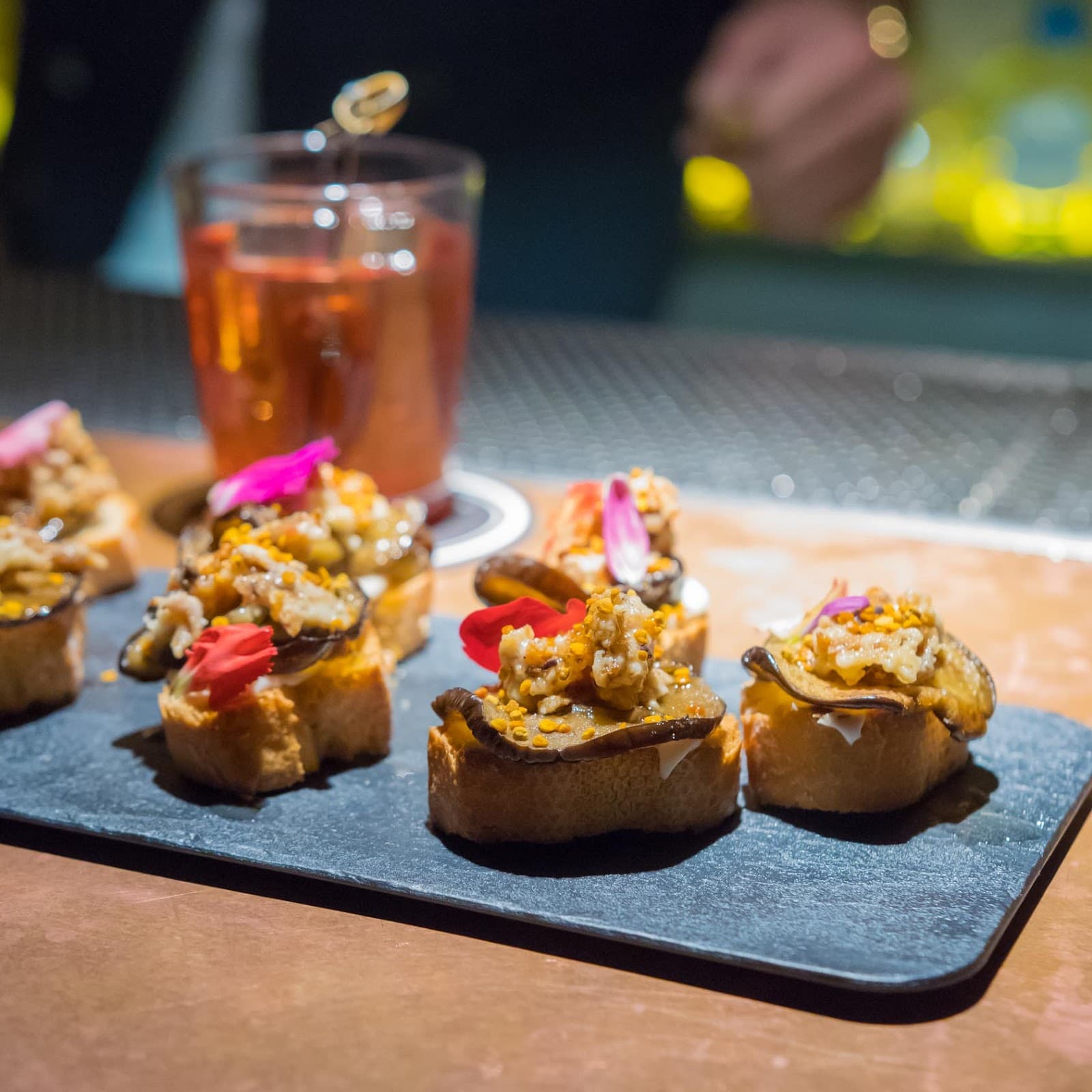 Close-up of gourmet appetizers with a cocktail in a dimly lit bar in Barcelona