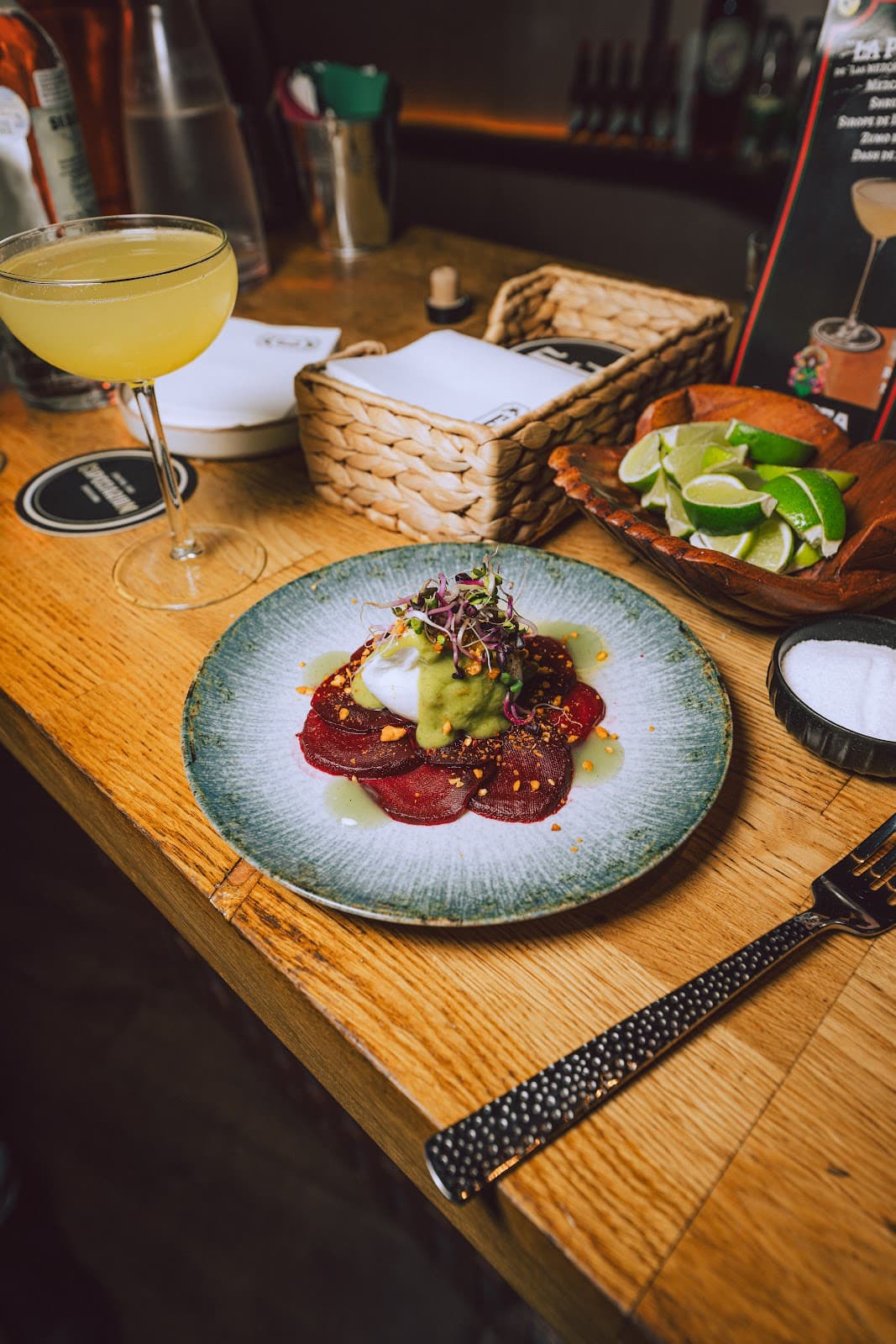 Artful cocktail and vibrant dish on a wooden bar counter with lime wedges in Barcelona