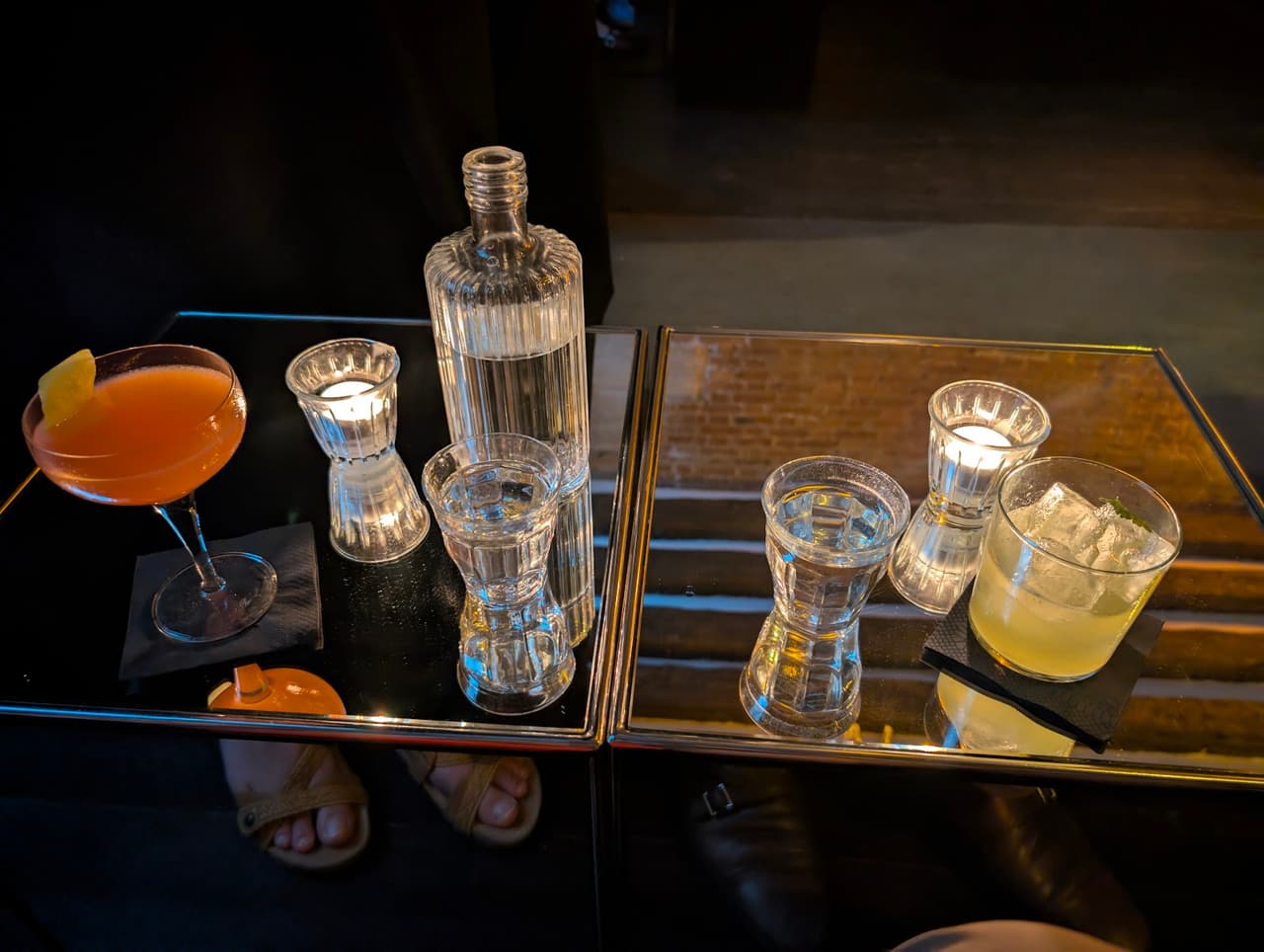 Cocktails on a mirrored table with candles in a dimly lit bar in Paris