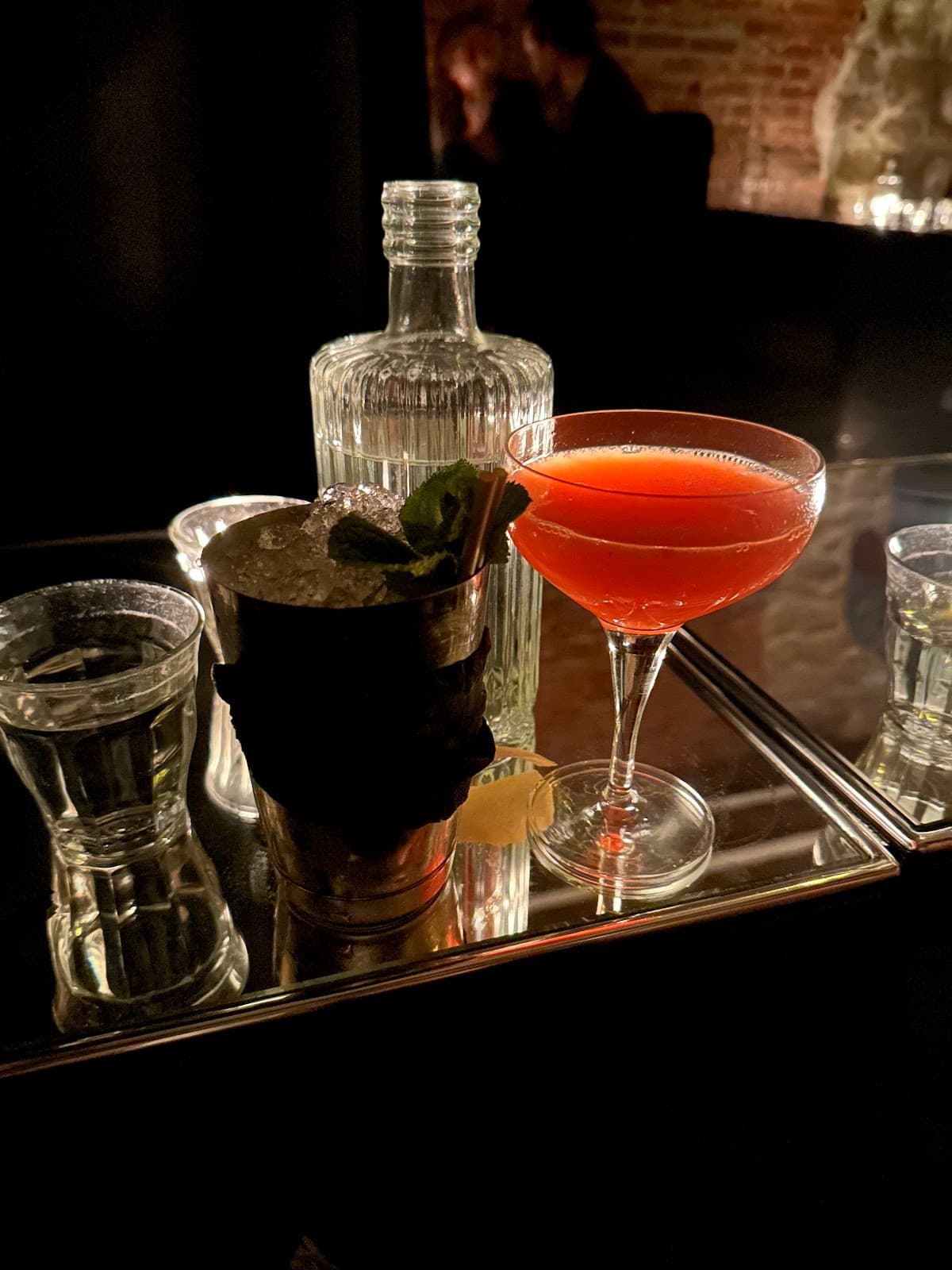 Cocktails on a dark bar counter with a brick wall backdrop in Paris