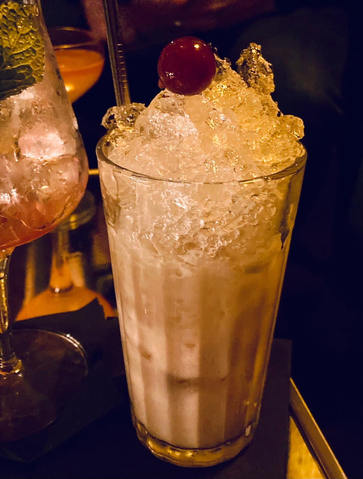 Cocktail with ice and cherry garnish on a dimly lit bar counter in Paris