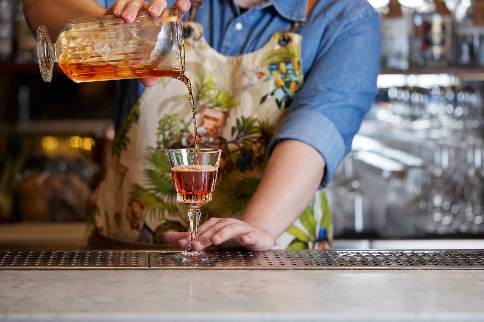 Bartender pouring cocktail with floral apron at marble bar in London