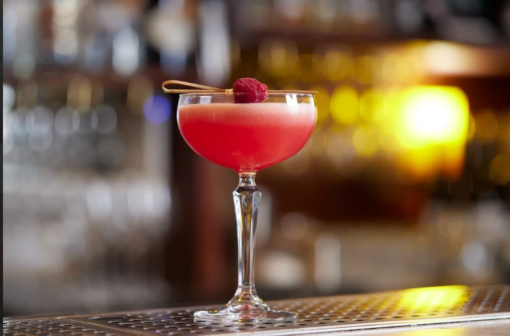 Red cocktail in a glass with a raspberry garnish on a bar counter in London