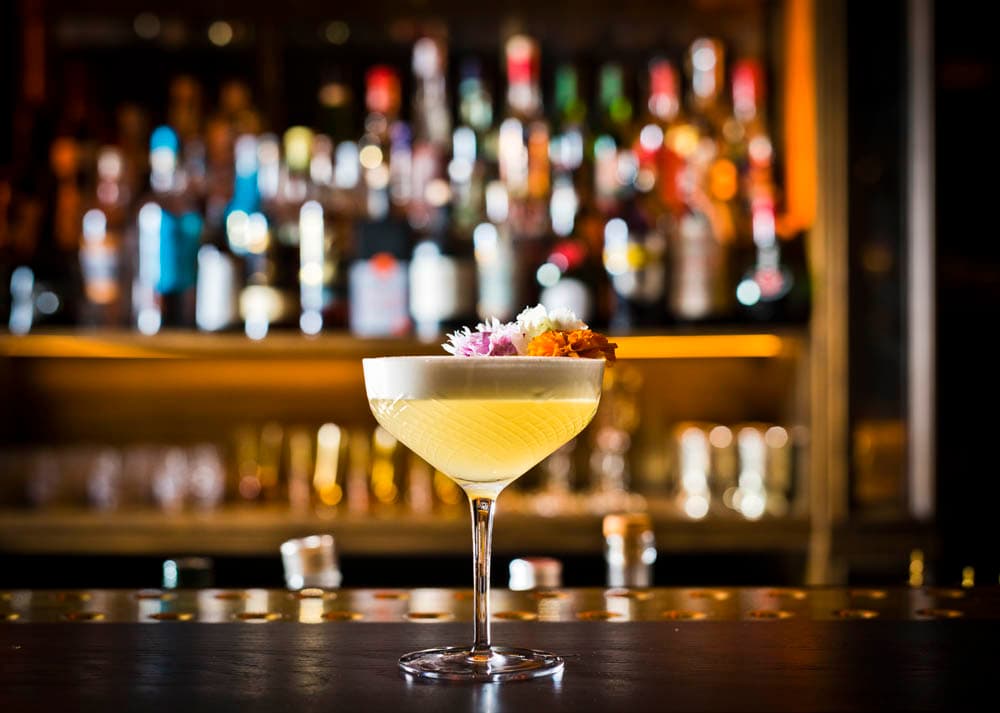 Elegant cocktail with foam and garnish at a bar with blurred bottles in background in London