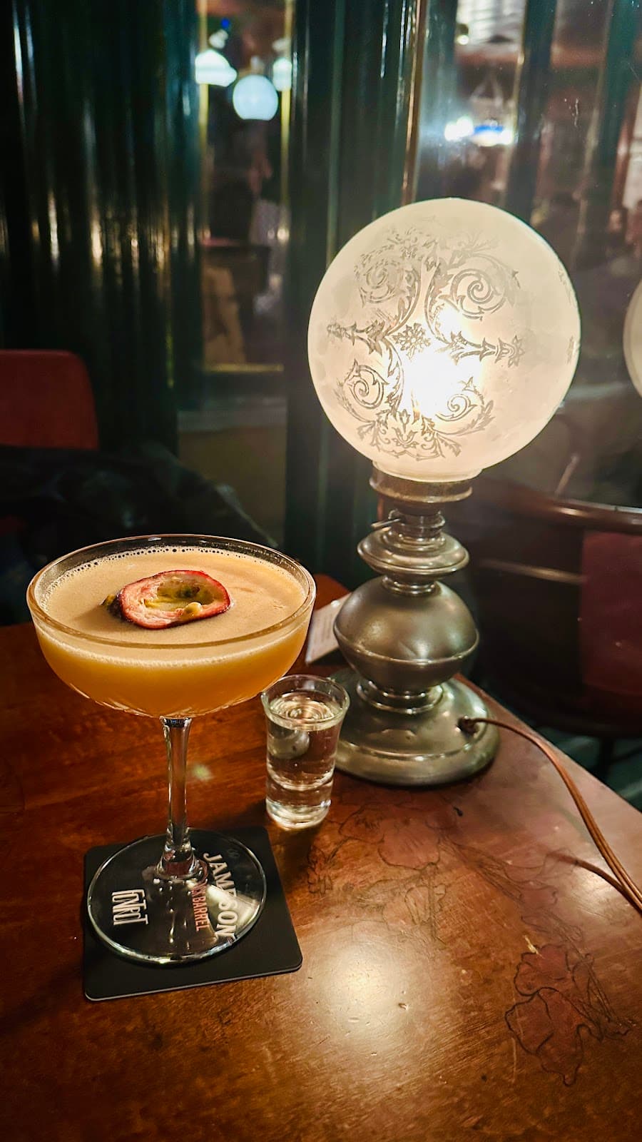 Cocktail with a slice of fruit beside a vintage lamp on a wooden table in Lisboa
