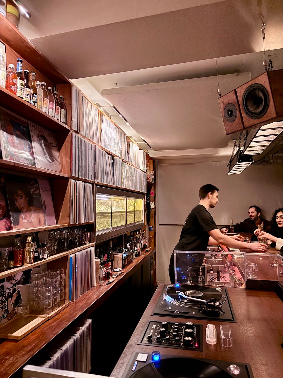 Trendy bar with vinyl records, turntables, and bartender serving drinks in Paris