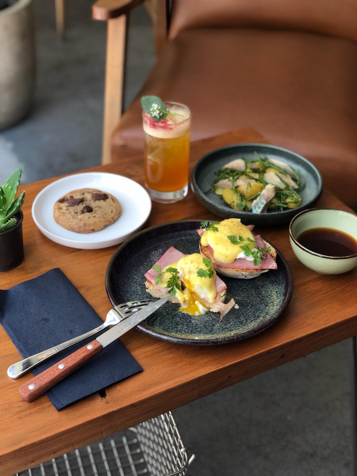 A brunch setup with eggs benedict, a cocktail, and a cookie on a wooden table in Paris
