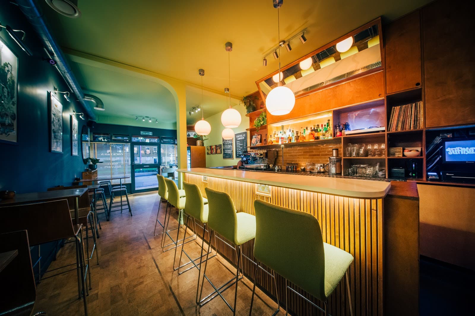 Well-lit bar interior with green chairs and hanging globe lights in London