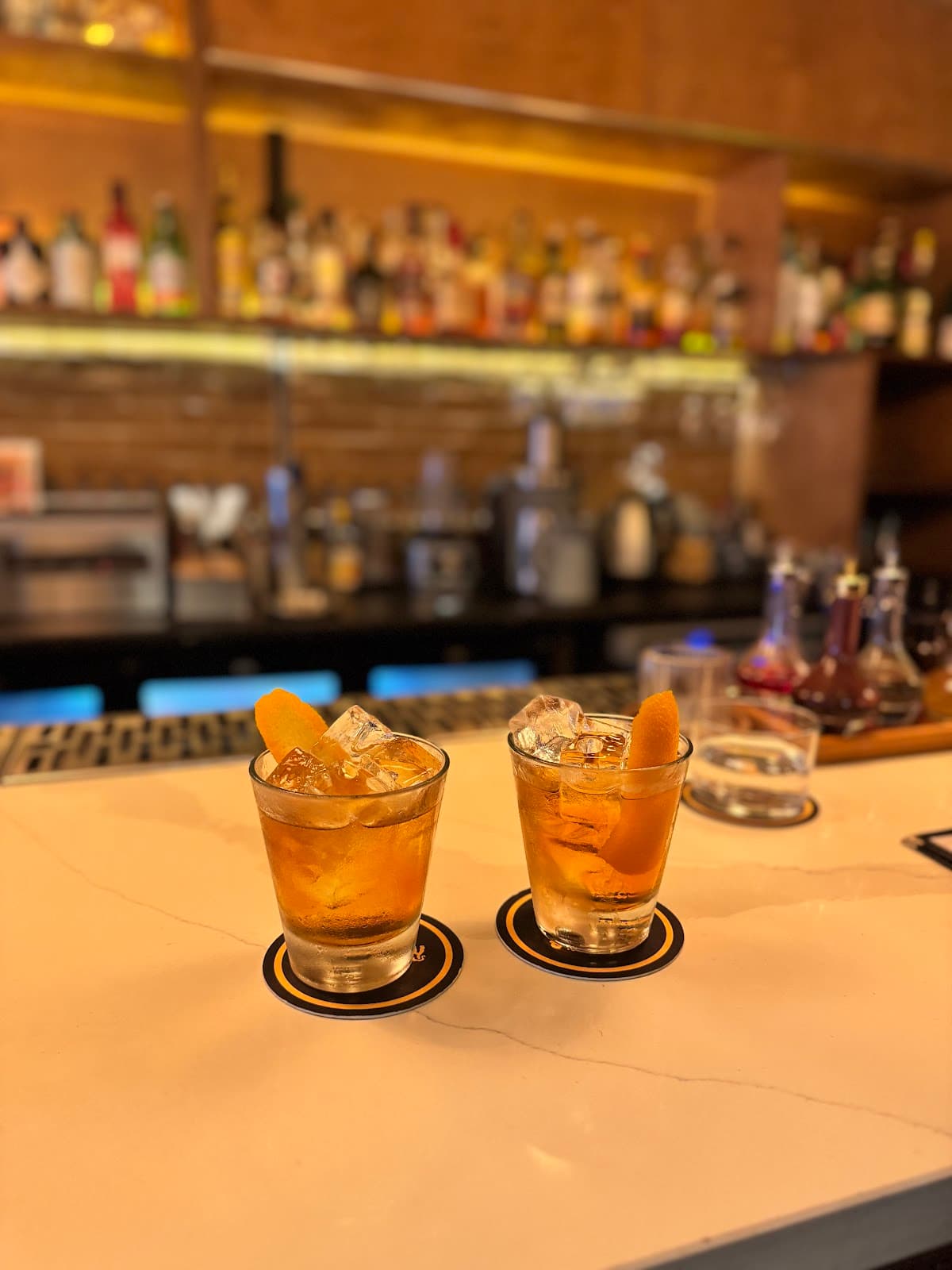 Two cocktails with orange garnishes on a bar counter in London