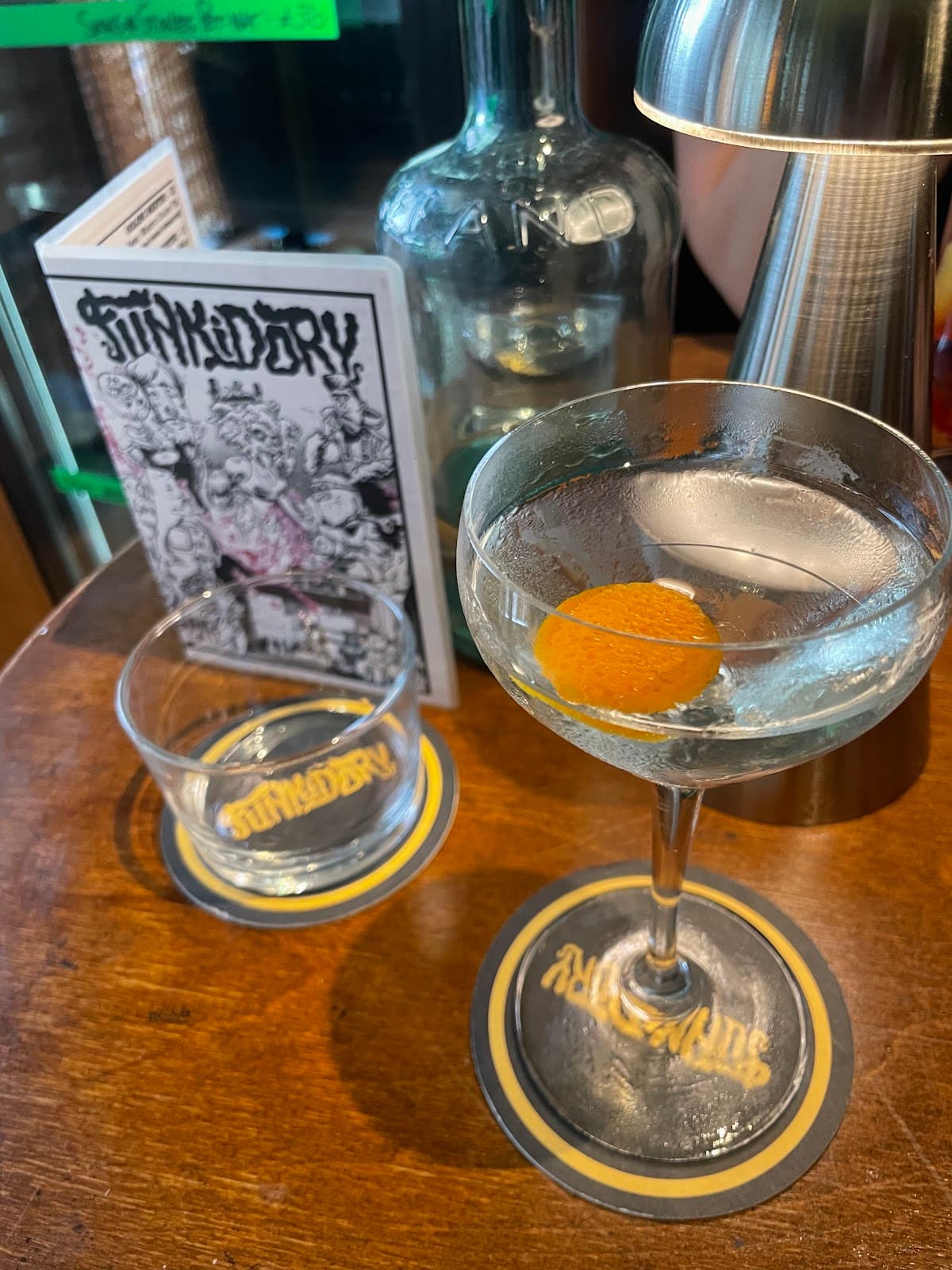 Cocktail with orange peel on bar table with menu and lamp in London