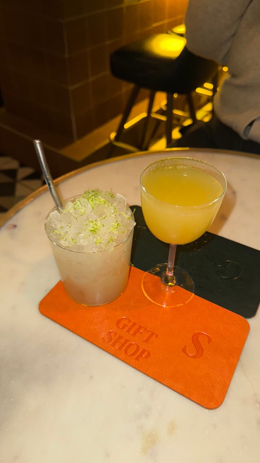 Two cocktails on a marble table with an orange coaster at Gift Shop bar in Toronto