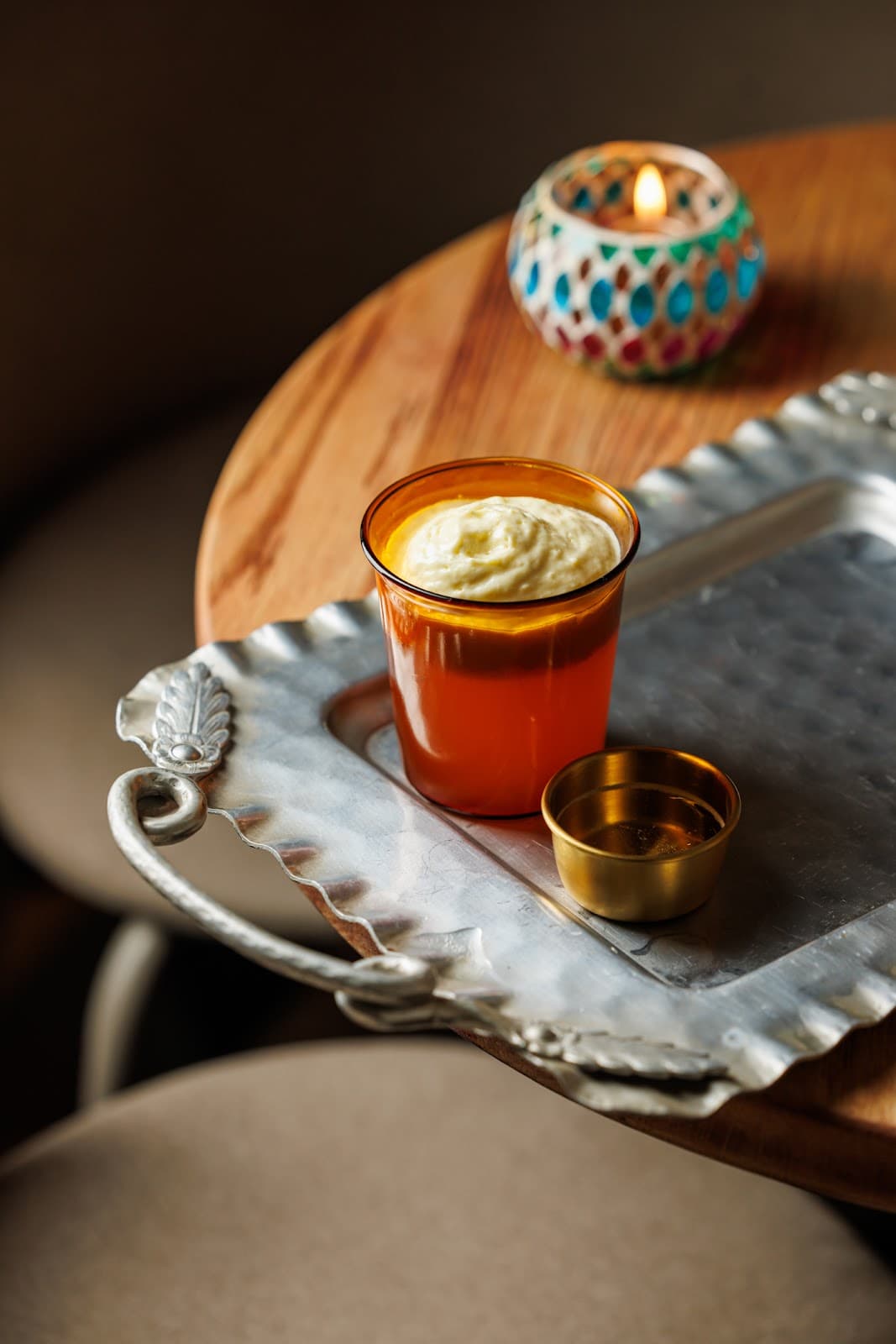 Cocktail with frothy top on a silver tray beside a lit candle. in Toronto
