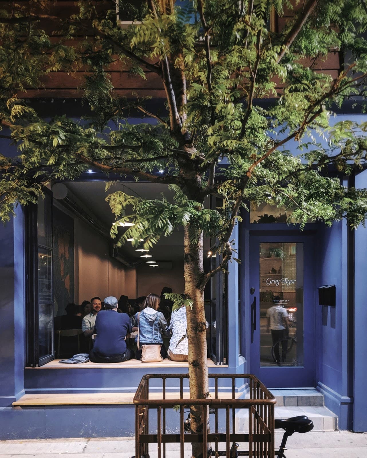 Exterior of cocktail bar Gray Tiger with window seating and a tree outside in Toronto