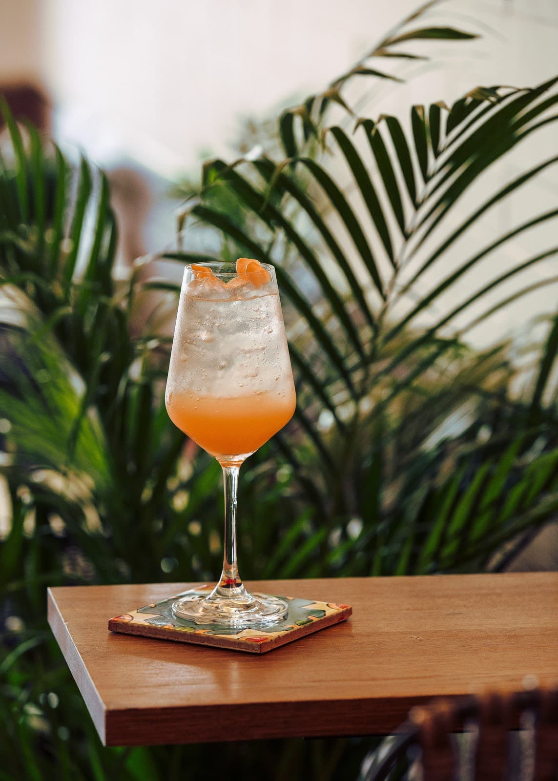 Orange cocktail in a stemmed glass on a wooden table with a leafy background in London