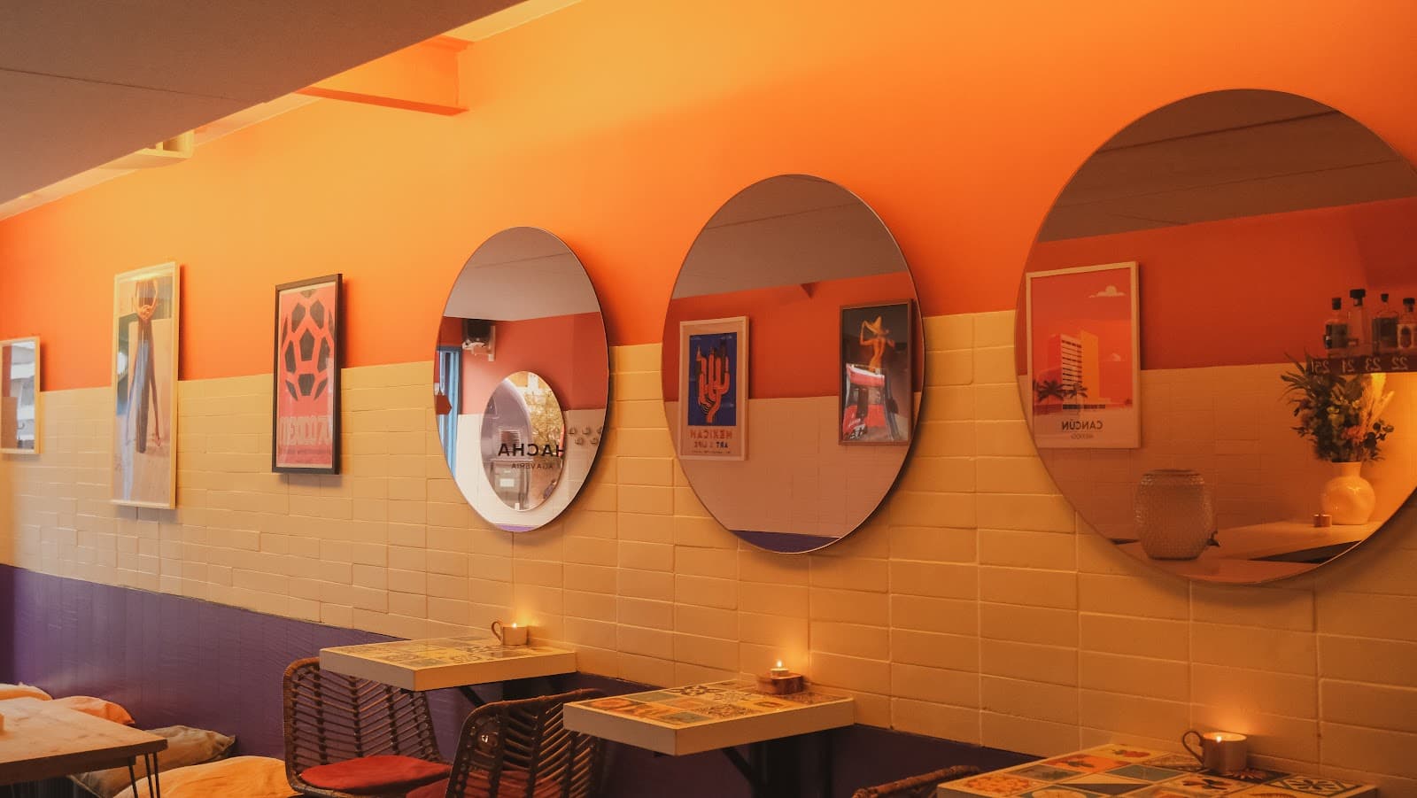Interior with round mirrors, orange walls, and small tables with candles in London