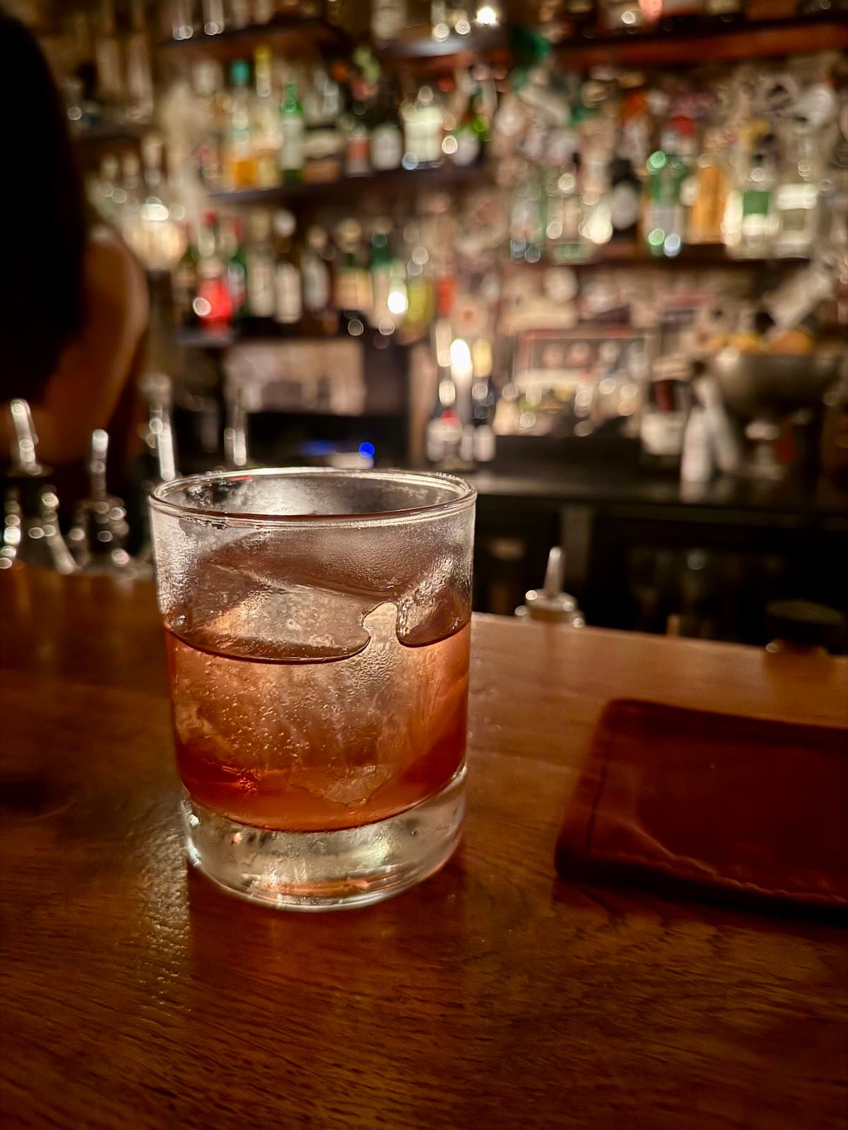 Close-up of a whiskey cocktail on a wooden bar counter in a dimly lit bar