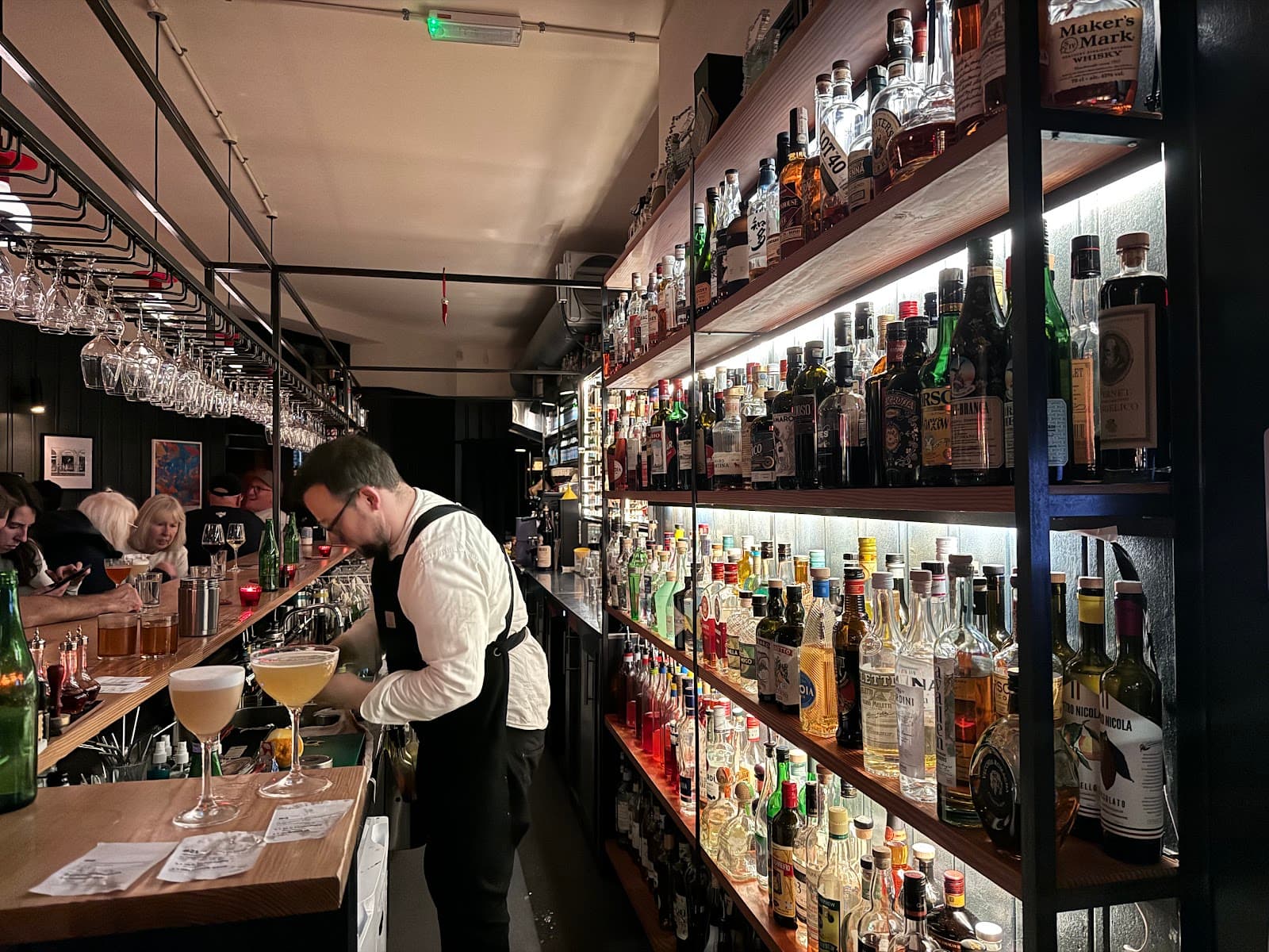 Bartender preparing drinks at a well-stocked bar with patrons seated