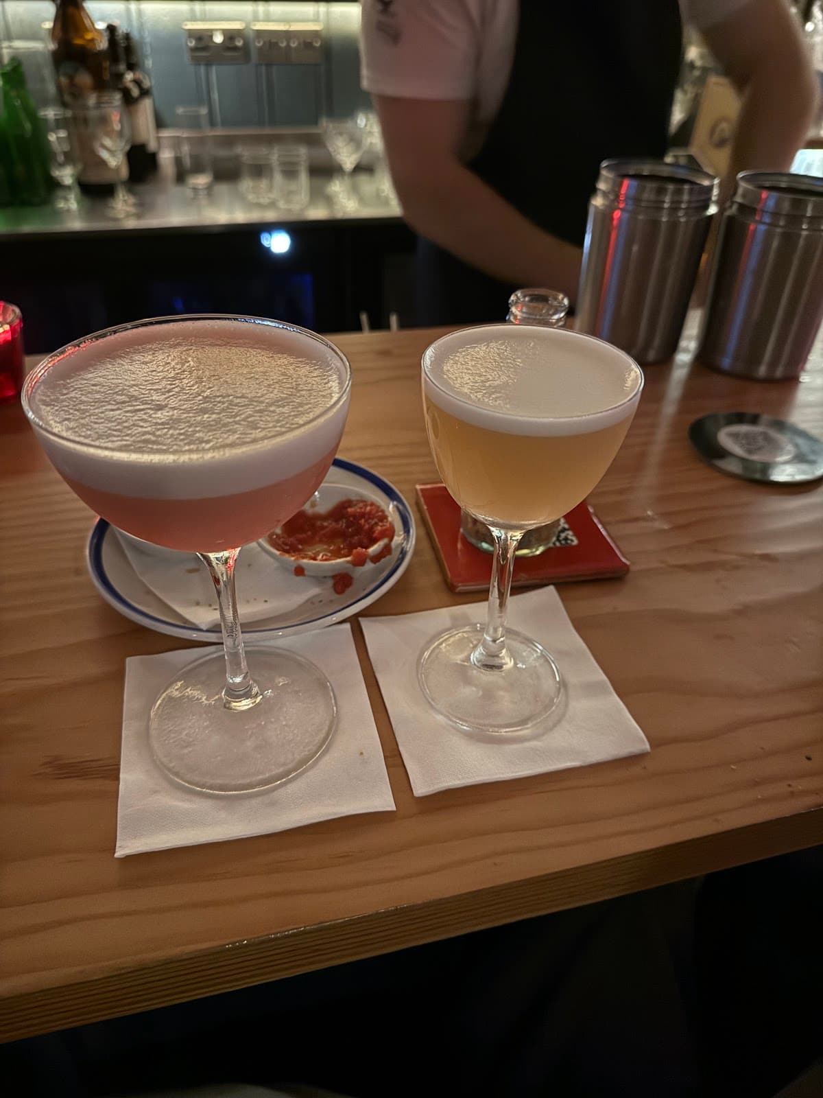 Two cocktails on a wooden bar with a bartender in the background in Edinburgh